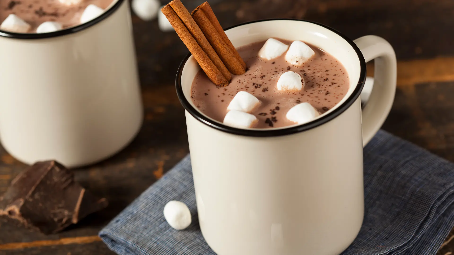 Eine Tasse heiße Schokolade, getoppt mit Marshmallows und Zimtstangen, auf einer Serviette auf einem Tisch.
