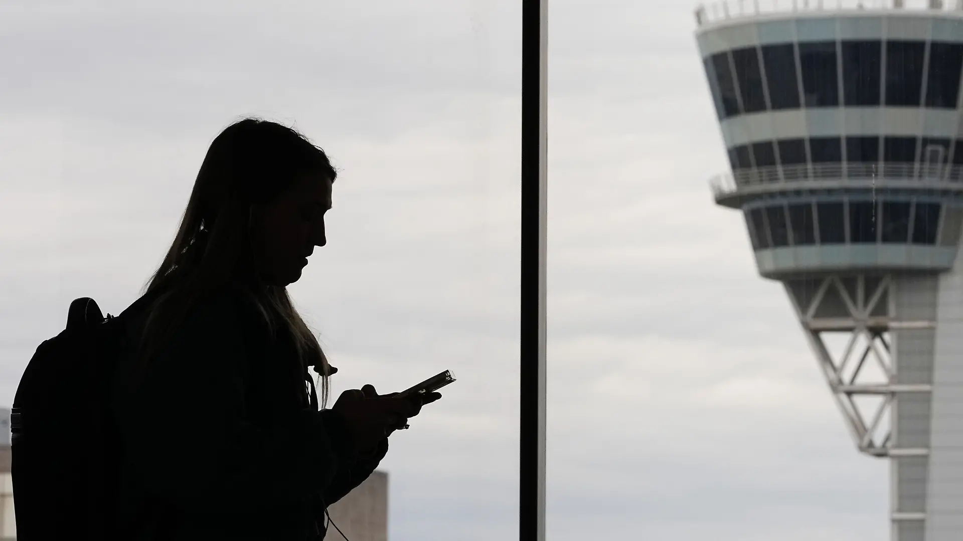 FILE - A traveler with a smartphone walks past an air traffic control tower at Philadelphia International Airport in Philadelphia on March 27, 2026. (AP Photo/Matt Rourke, File)