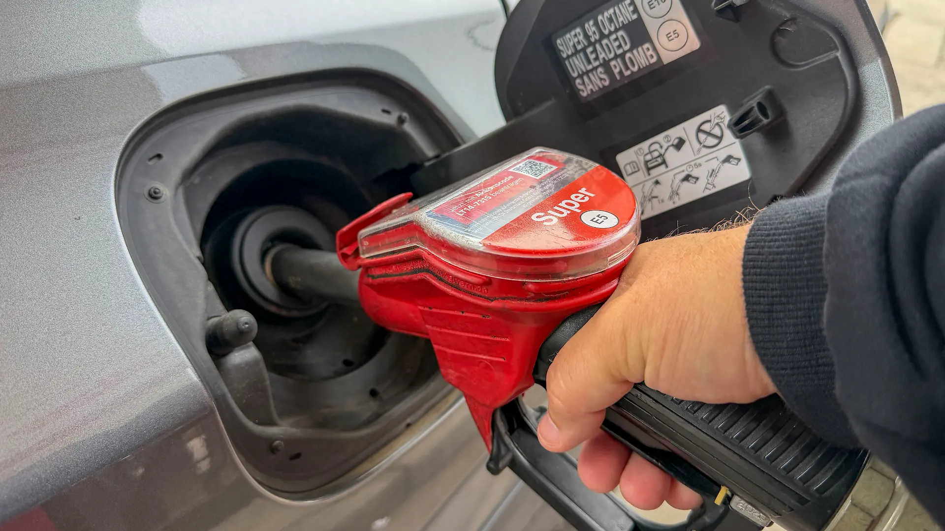 Ein Autofahrer hält eine Zapfpistole beim Betanken eines Autos an einer Tankstelle. Das Symbolfoto steht für Tanken, Kraftstoff, Benzinpreise, Mobilität und steigende Kosten im Straßenverkehr.