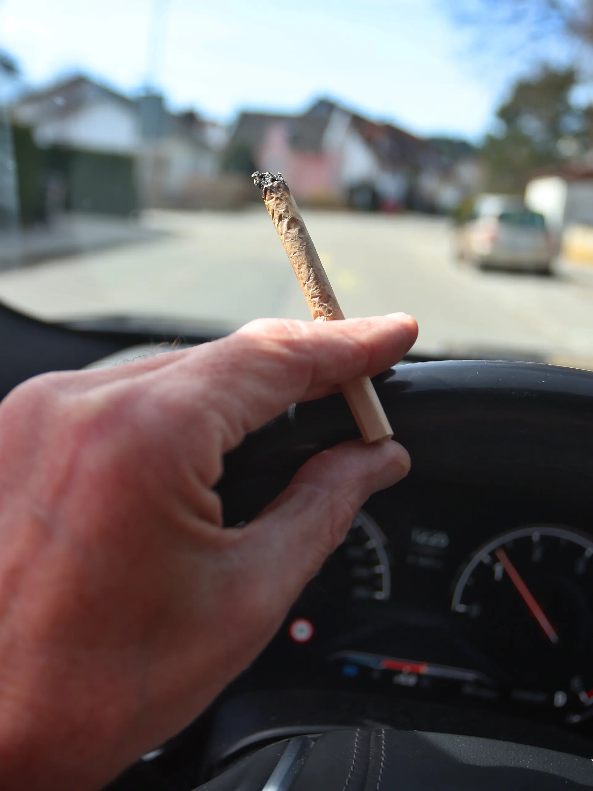 Ein Mann sitzt mit einem Joint zwischen den Fingern am Steuer eines Autos. Der Bundesrat hatte am 22. März den Weg zur Teil-Legalisierung von Cannabis zum 1. April freigemacht.