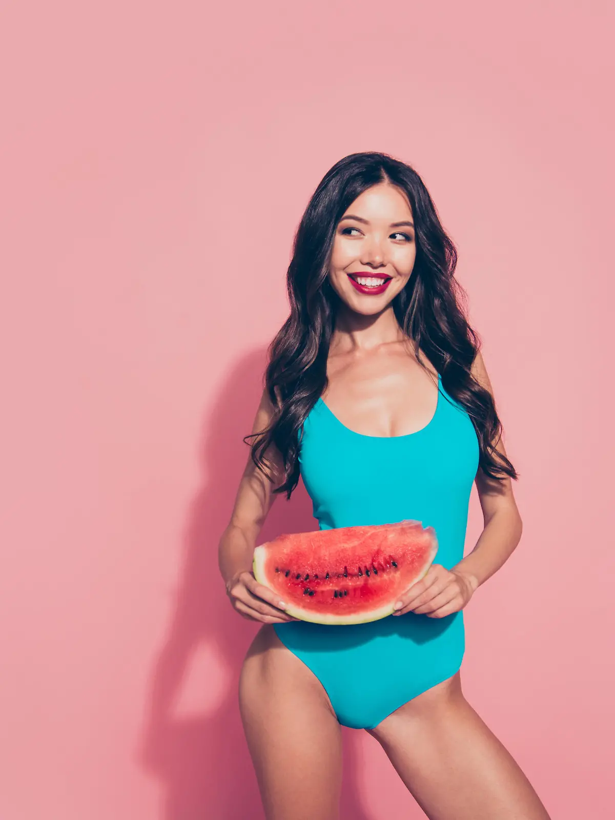 Frau im Badeanzug hält eine Wassermelone in der Hand.