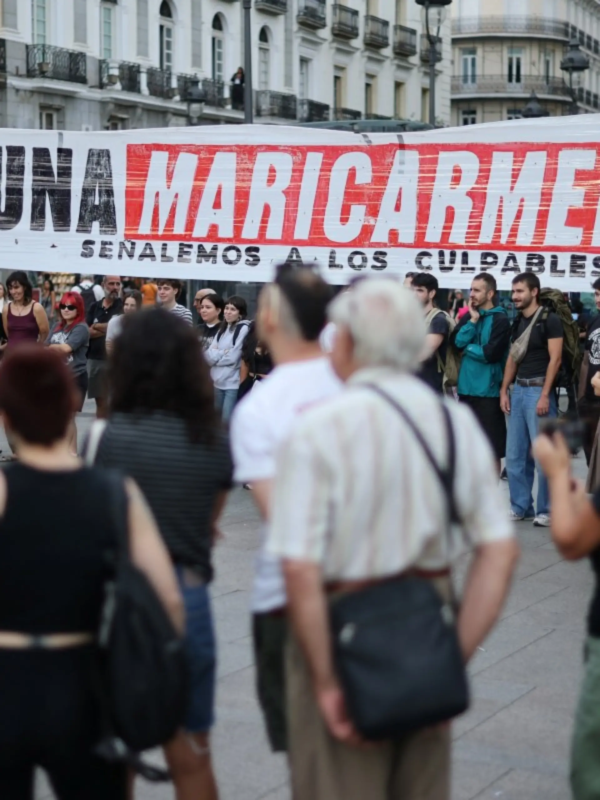 People gather next to a banner reading 'Not a single more Maricarmen' - in reference to an 87-year-old evicted from her Madrid home - as demonstrators camp to protest against evictions and the housing crisis in front of the Presidency of the Community of Madrid on the Puerta del Sol plaza in Madrid on September 27, 2026. Spain's main tenants' unions on September 25 urged the government to pass a new law to tackle the country's housing crisis after an 87-year-old was evicted from her Madrid home, sparking nationwide protests. (Photo by Thomas COEX / AFP)