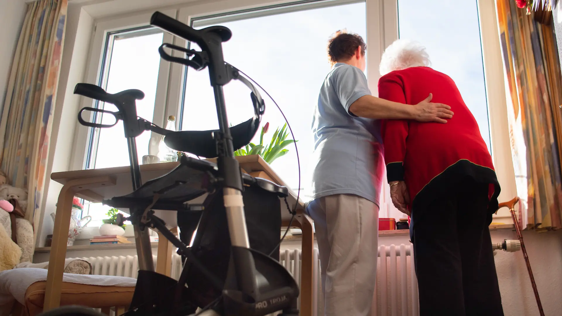 Eine Pflegerin (l) und eine Heimbewohnerin schauen zusammen aus einem Fenster im Wohnbereich des Pflegeheims. Im Vordergrund steht ein Rollator. (zu dpa: «Aus für Pflegegrad 1? - Gut 58.000 Sachsen wären betroffen») +++ dpa-Bildfunk +++