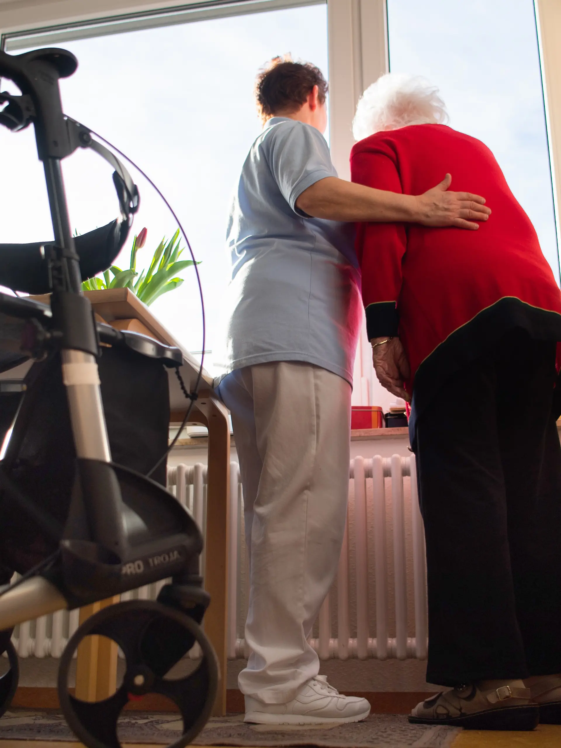 Eine Pflegerin (l) und eine Heimbewohnerin schauen zusammen aus einem Fenster im Wohnbereich des Pflegeheims. Im Vordergrund steht ein Rollator. (zu dpa: «Aus für Pflegegrad 1? - Gut 58.000 Sachsen wären betroffen») +++ dpa-Bildfunk +++