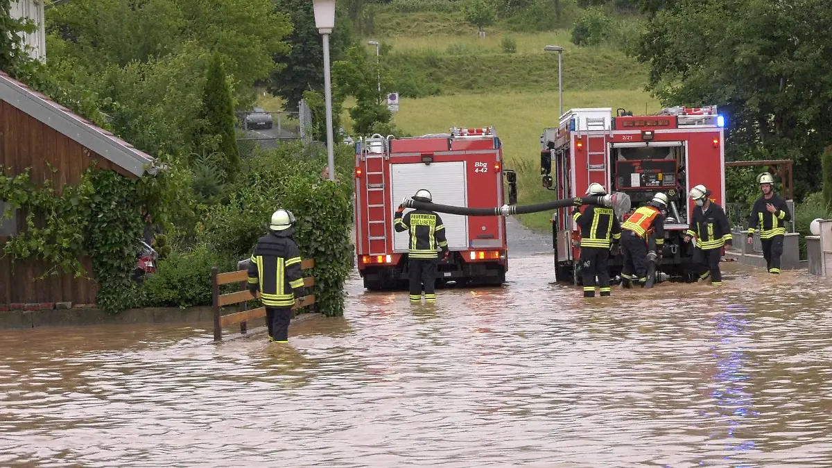 29.06.2021, Hessen, Breuberg (Odenwald): Einsatzkräfte der Feuerwehr stehen auf einer durch ein Unwetter überfluteten Straße. Foto: Alexander Keutz/Keutz TV-NEWS/dpa +++ dpa-Bildfunk +++