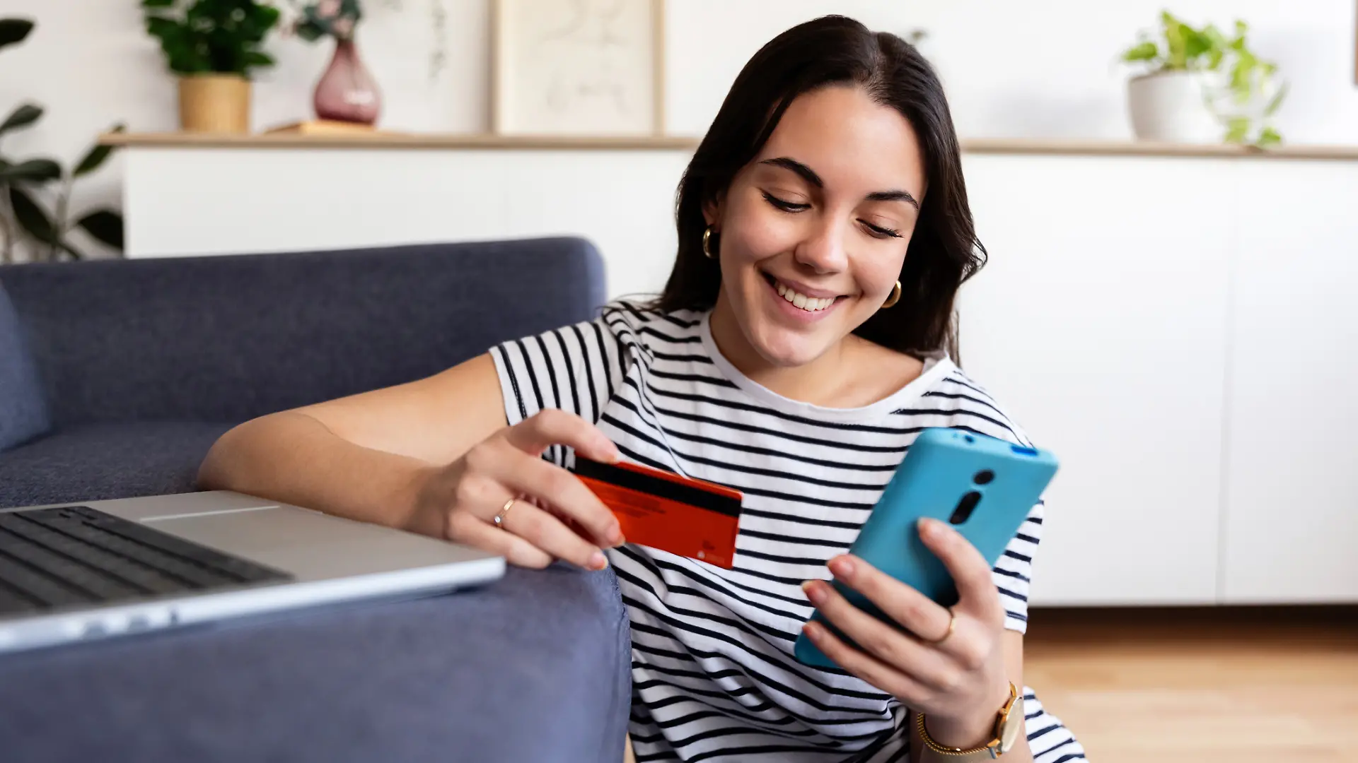 Frau schaut freudig auf ihr Smartphone und hat eine Kreditkarte in der Hand.