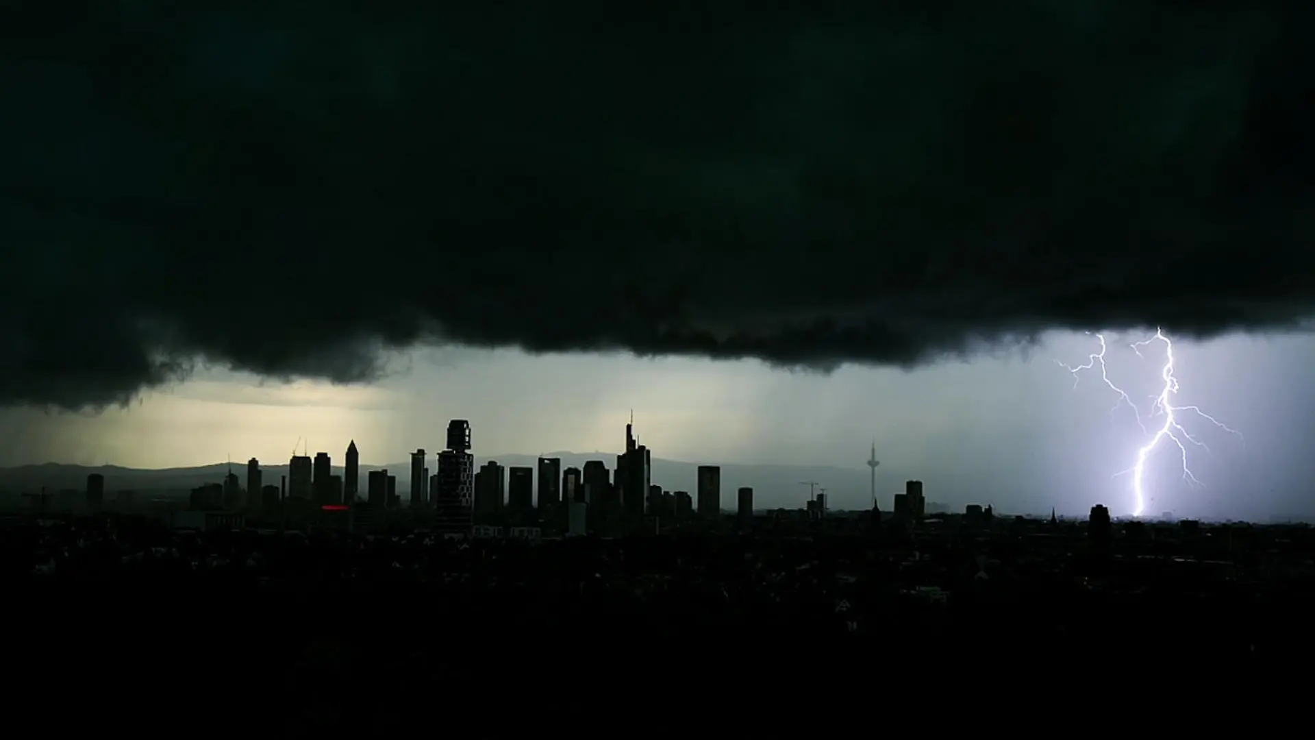 dpatopbilder - 29.06.2021, Hessen, Frankfurt/Main: Tiefschwarze Gewitterwolken verdunkeln den Himmel über der Frankfurter Innenstadt und seinen markanten Hochhäusern, während sich ein Blitz entlädt. Foto: Arne Dedert/dpa +++ dpa-Bildfunk +++