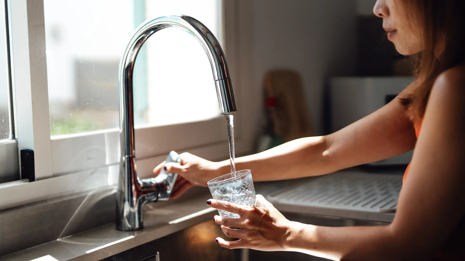 Eine Frau füllt sich ein Wasserglas am Wasserhahn auf.