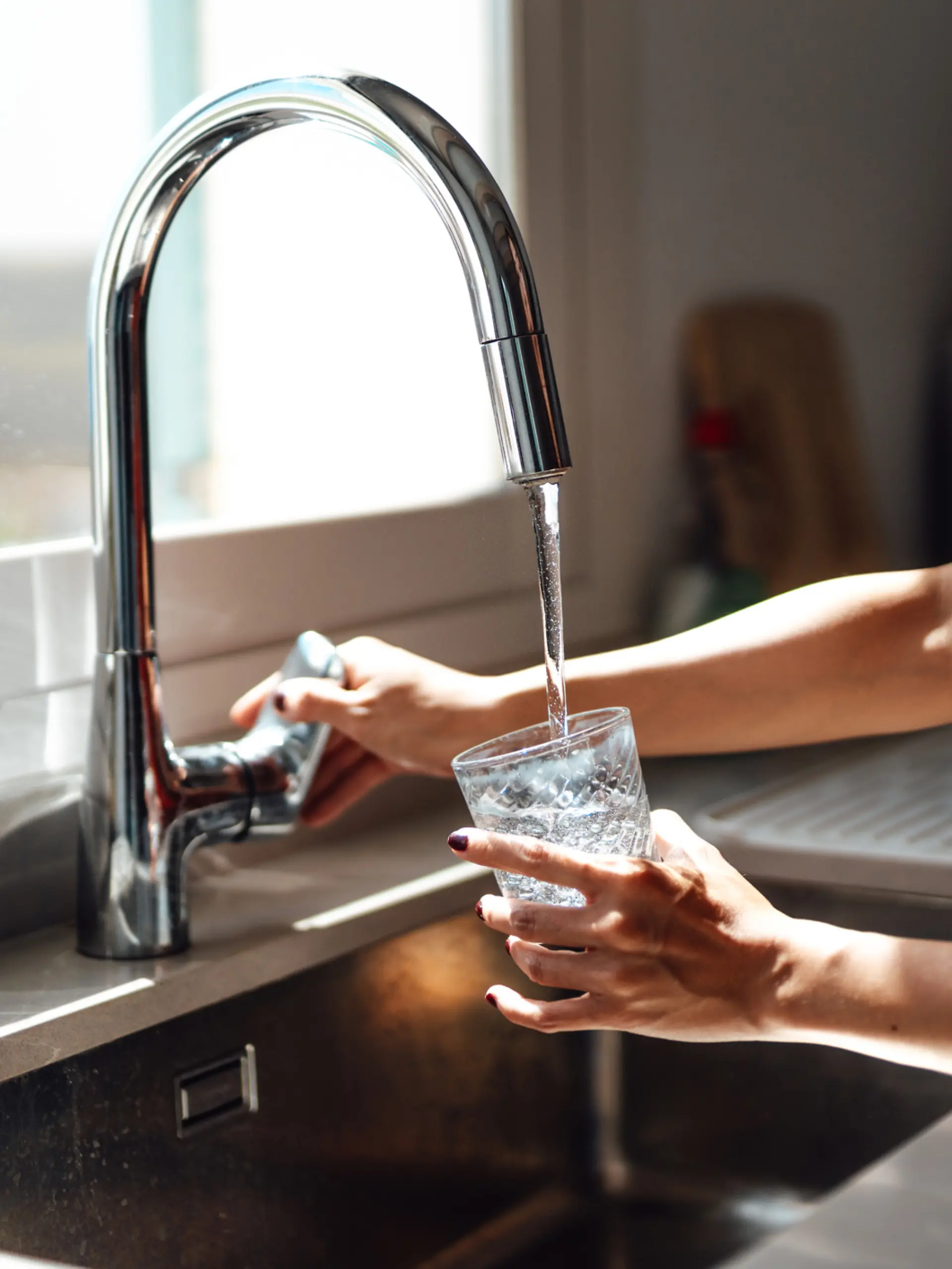 Eine Frau füllt sich ein Wasserglas am Wasserhahn auf.