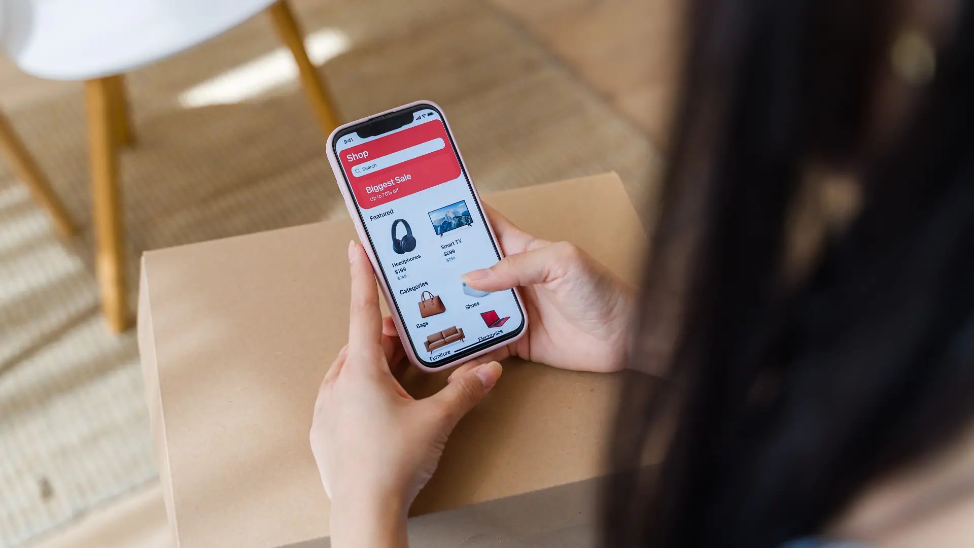 Frauenhände, die ein Smartphone halten und in einer E-Commerce-App über einem Versandkarton stöbern