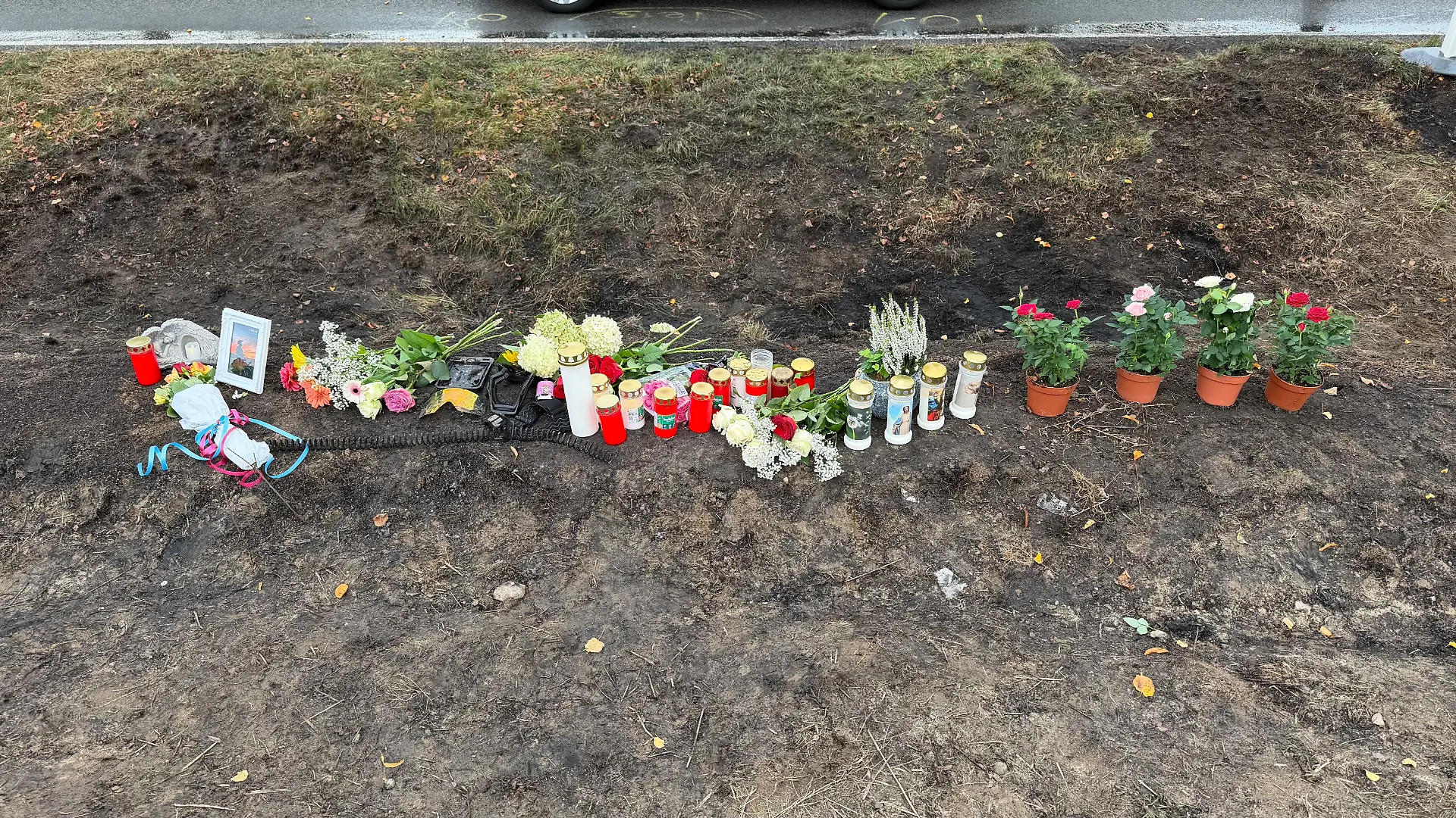 Zwischen Blumen und Kerzen liegen auch eine Schutzbrille und Fahrzeugteile – persönliche Erinnerungsstücke der Opfer.