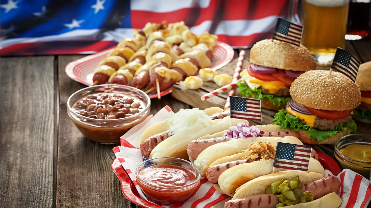 Auf einem Gartentisch stehen typisch US-amerikanische Speisen, wie Hamburger, Hot Dogs und Co.