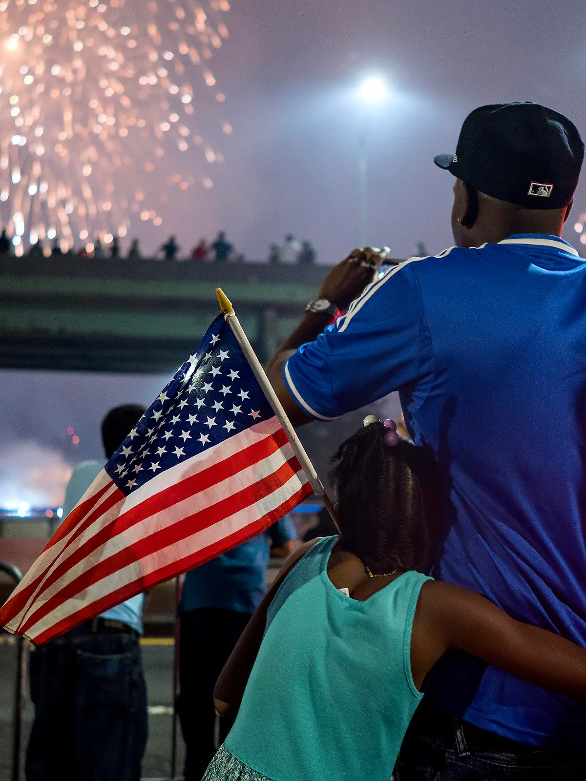 FILE - In this July 4, 2018 file photo, Deon Stewart and his daughter Semiyah, of New York, join other spectators as they watch a fireworks display on the east side of Manhattan, part of Independence Day festivities in New York. The Macy's Fourth of July fireworks show will return to New York City this year. (AP Photo/Craig Ruttle, File)