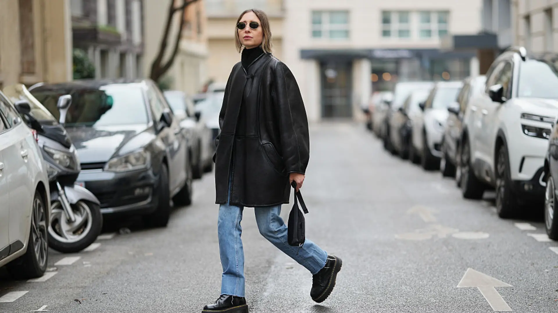 Emy Venturini kombiniert Dr. Martens zu einem schwarzen Mantel, Sonnenbrille und Straight-Leg-Jeans.
