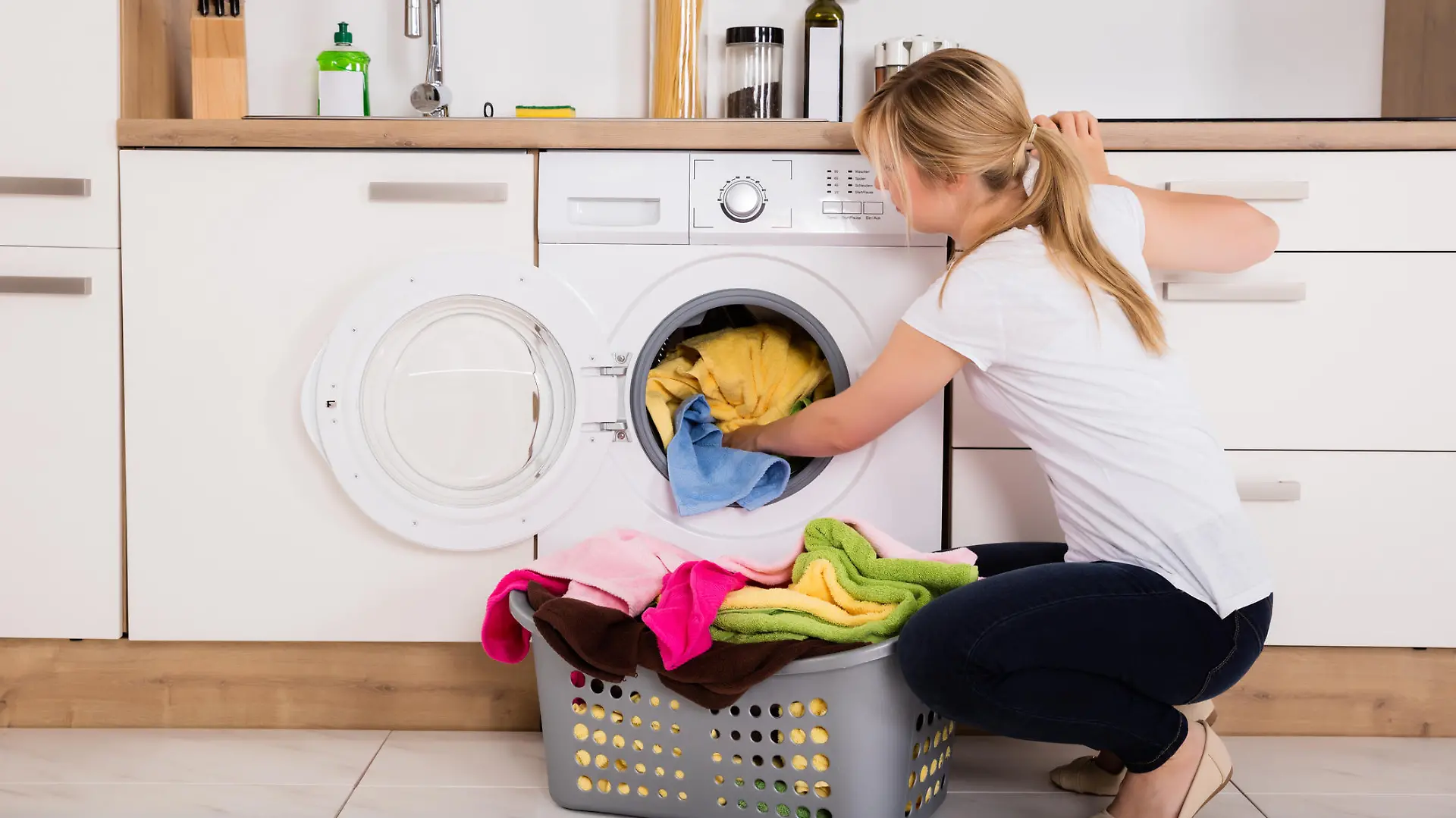 Young Woman Loading Clothes Into Washing Machine In Kitchen