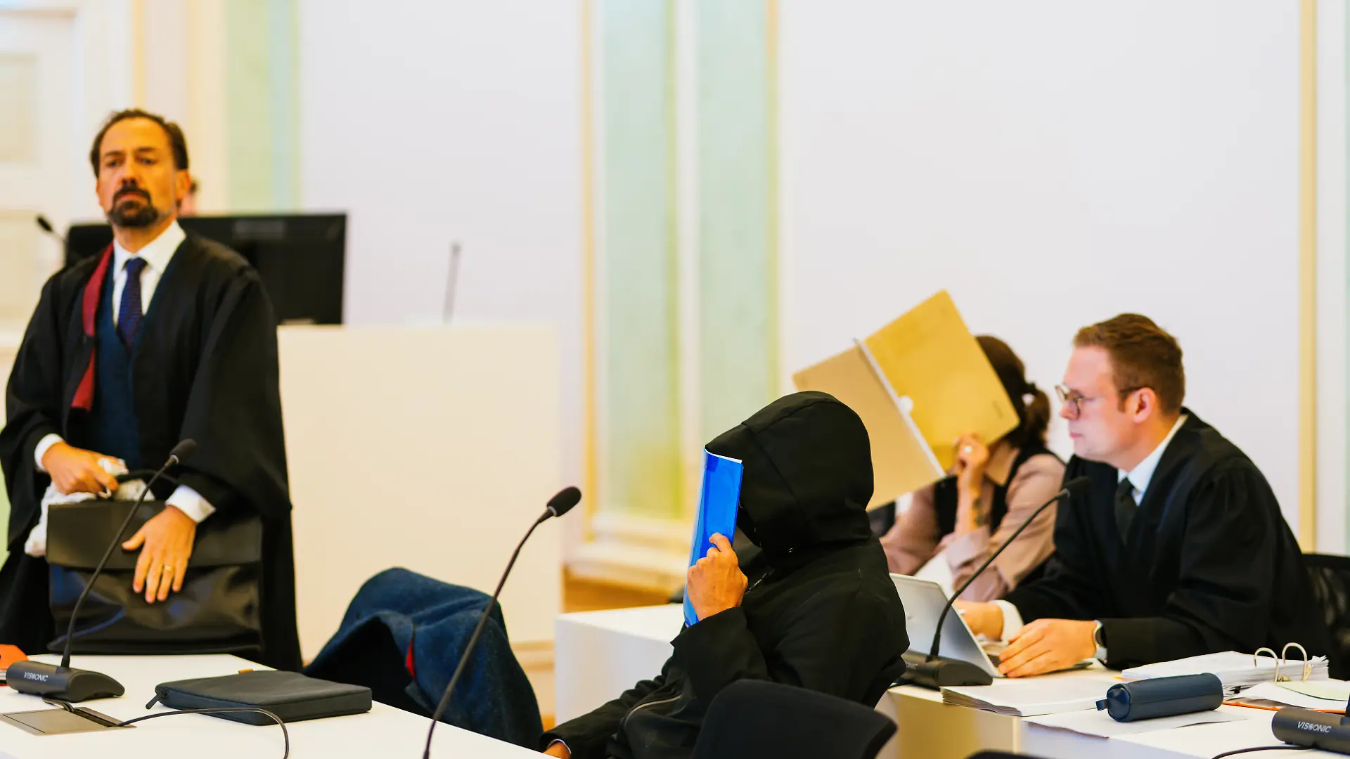 Zwei Angeklagte sitzen zwischen ihren Verteidigern Nico Schmid (r) und Jan-Georg Wennekers (l). Einem angeklagten Ehepaar werden neben 50 Fällen von Diebstahl, beziehungsweise wegen Beihilfe, mindestens 250 Fälle vorgeworfen. Der Ehemann war nach Angaben des Gerichts bis Ende Oktober 2024 als Bestatter beim Eigenbetrieb Friedhöfe der Stadt Freiburg angestellt. Ihm wird vorgeworfen, von 2013 an Zahngold von Leichen entwendet zu haben, die verbrannt werden sollten - teilweise mit grober Gewalt. Außerdem soll er den Leichen Schmuck, Uhren und sonstige Wertgegenstände abgenommen haben. Seine Frau soll ihn bei den Taten unterstützt haben. (zu dpa: «Zahngold von Toten geklaut? Bestatter droht Haftstrafe») +++ dpa-Bildfunk +++