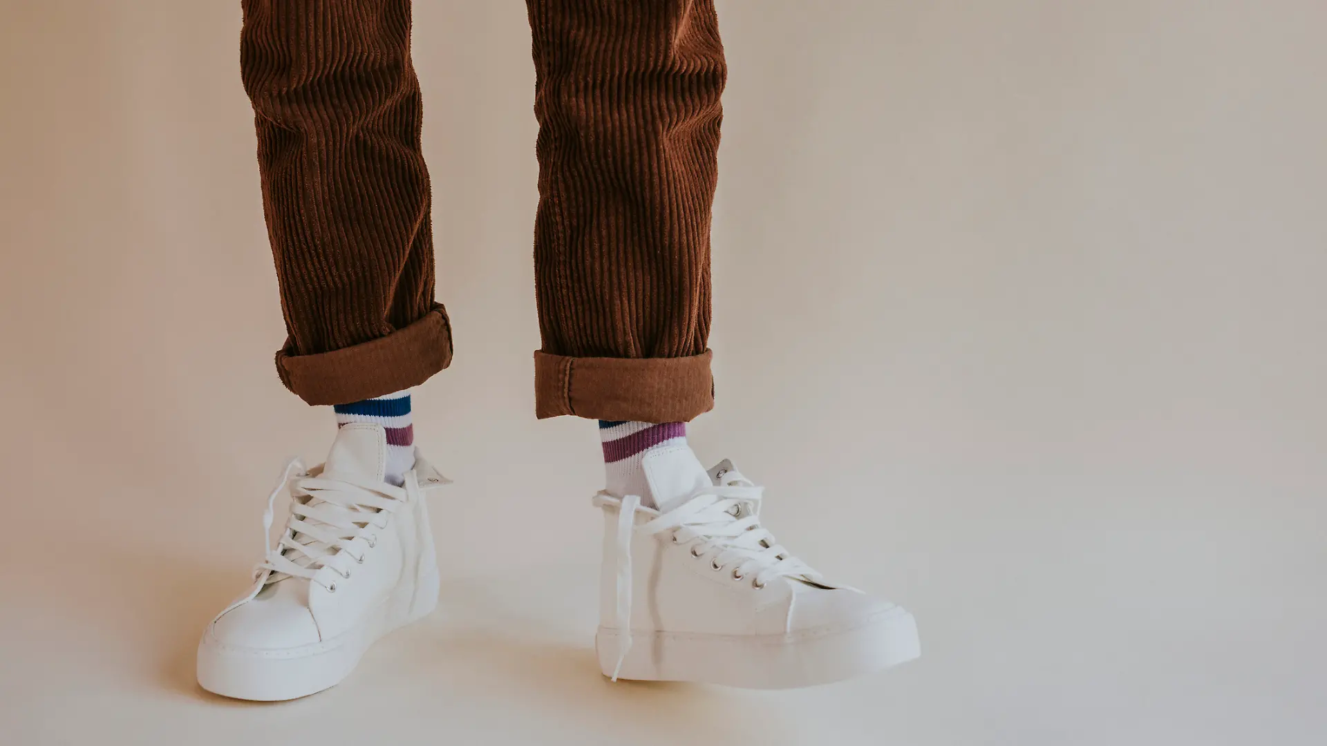 Ein Mann trägt eine braune Cordhose und weiße Sneaker.