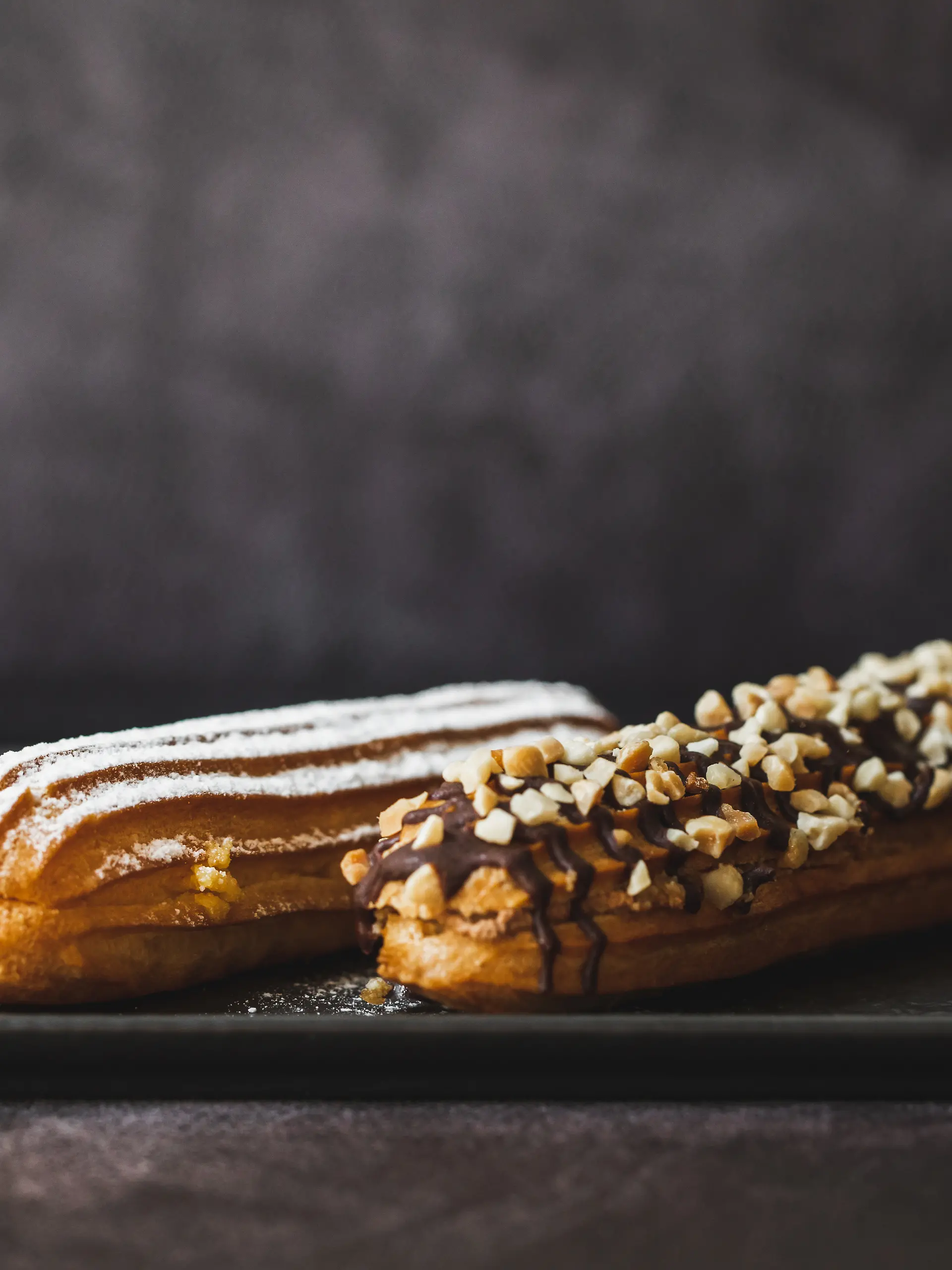 Zwei Eclairs auf einem Teller vor dunklem Hintergrund.