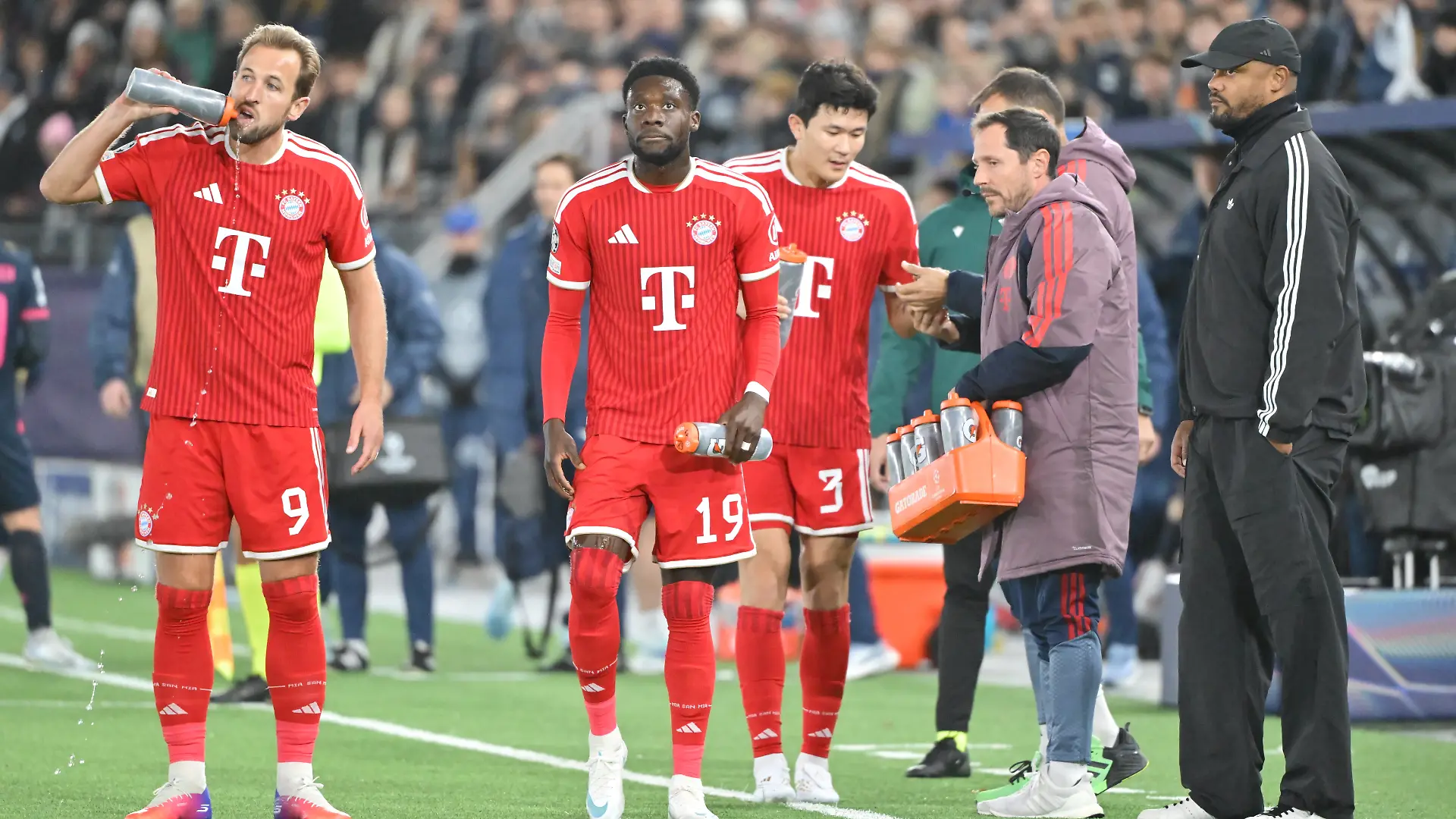 Fußball, Männer: Champions League, Viking Stavanger - Bayern München, Vorrunde, 2. Spieltag, im Stadion Lyse Arena. Harry Kane (FC Bayern München, l-r), Alphonso Davies (FC Bayern München) und Min-Jae Kim (FC Bayern München) trinken am Spielfeldrand. Vincent Kompany (r), Trainer vom FC Bayern München, schaut ihnen zu.