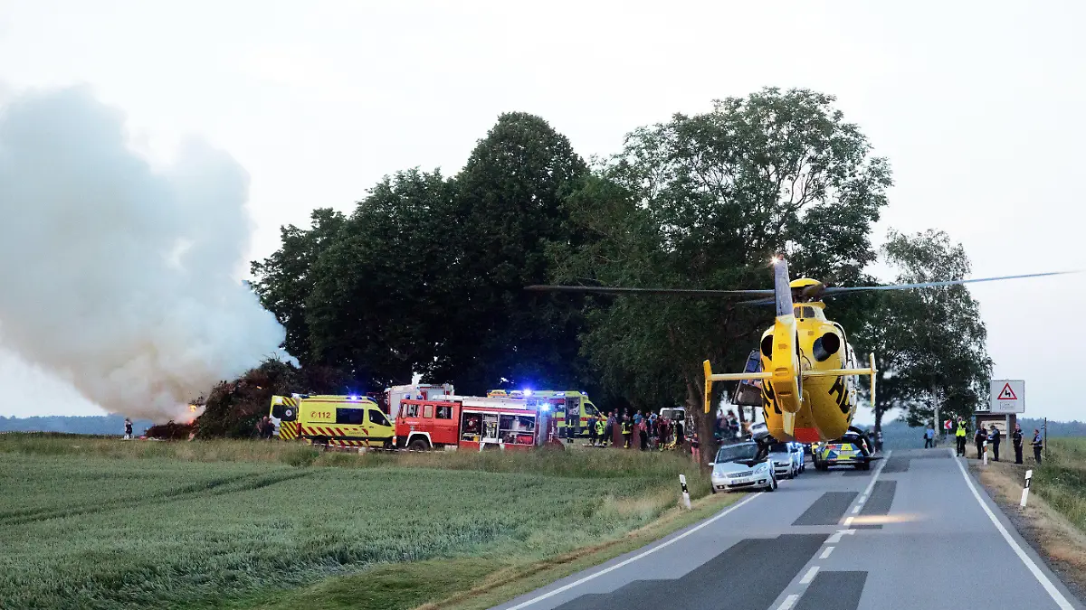 26.06.2021, Sachsen, Steinigtwolmsdorf: Das Feuer brennt noch, als einer von vier Rettungshubschraubern Verletze ins Krankenhaus fliegt. Beim Anzünden eines Holzhaufen am Abend hat es eine starke Verpuffung gegeben. Es gab mindestens acht Verletzte. Foto: Rocci Klein/dpa +++ dpa-Bildfunk +++