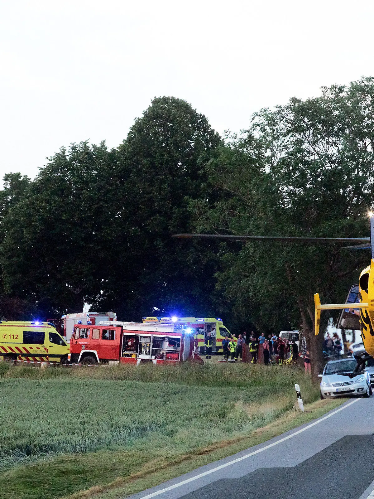 26.06.2021, Sachsen, Steinigtwolmsdorf: Das Feuer brennt noch, als einer von vier Rettungshubschraubern Verletze ins Krankenhaus fliegt. Beim Anzünden eines Holzhaufen am Abend hat es eine starke Verpuffung gegeben. Es gab mindestens acht Verletzte. Foto: Rocci Klein/dpa +++ dpa-Bildfunk +++