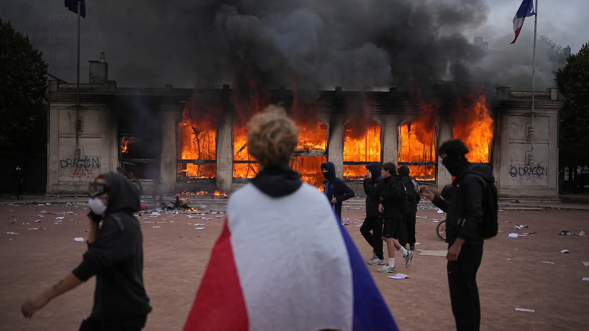 A protester wraps a French flag around them in front of the burning tourism office during a demonstration against rising living costs and in solidarity with students’ grievances in Lyon, France, Saturday, Oct. 17, 2026.(AP Photo/Laurent Cipriani)