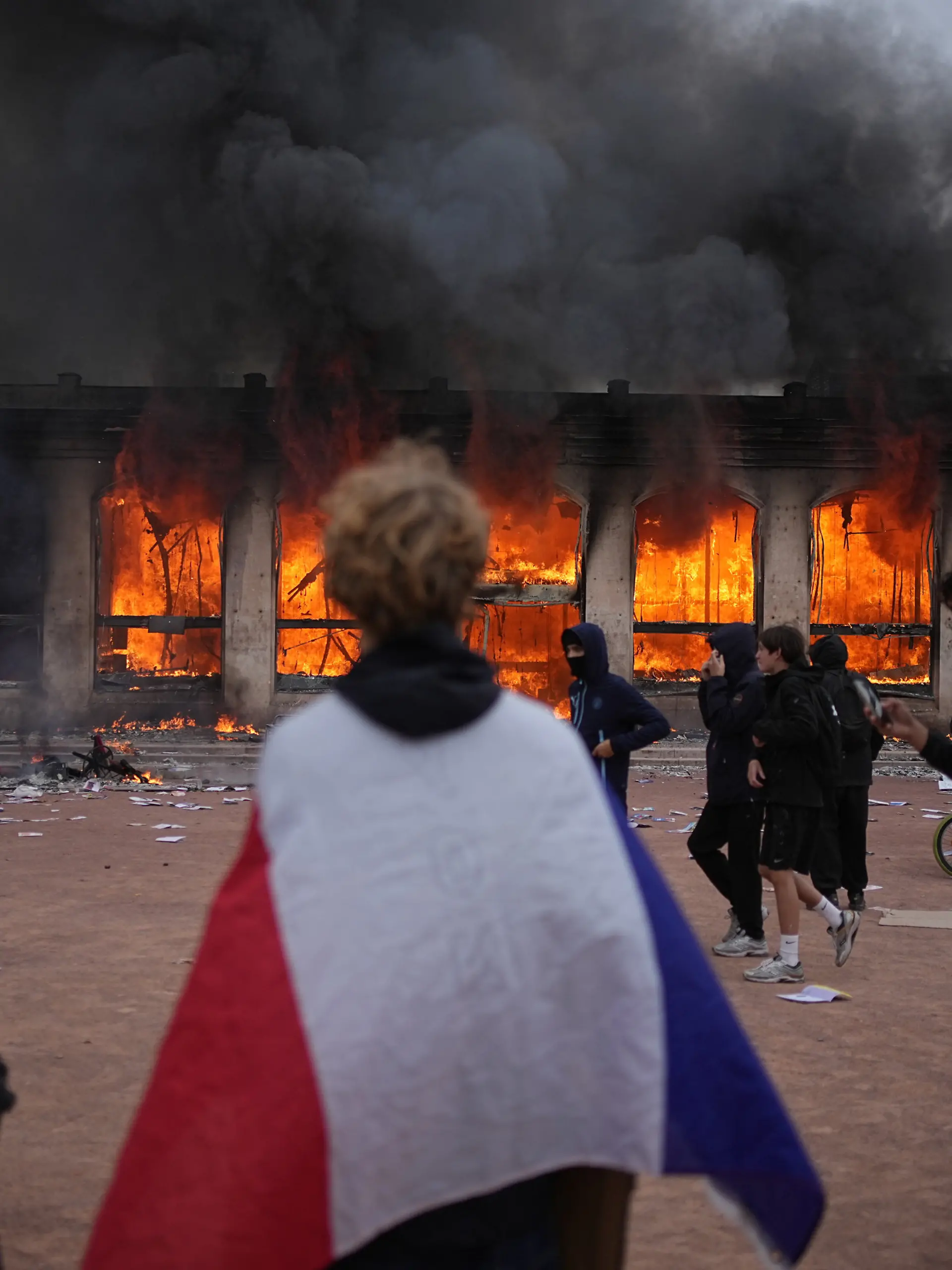 A protester wraps a French flag around them in front of the burning tourism office during a demonstration against rising living costs and in solidarity with students’ grievances in Lyon, France, Saturday, Oct. 17, 2026.(AP Photo/Laurent Cipriani)