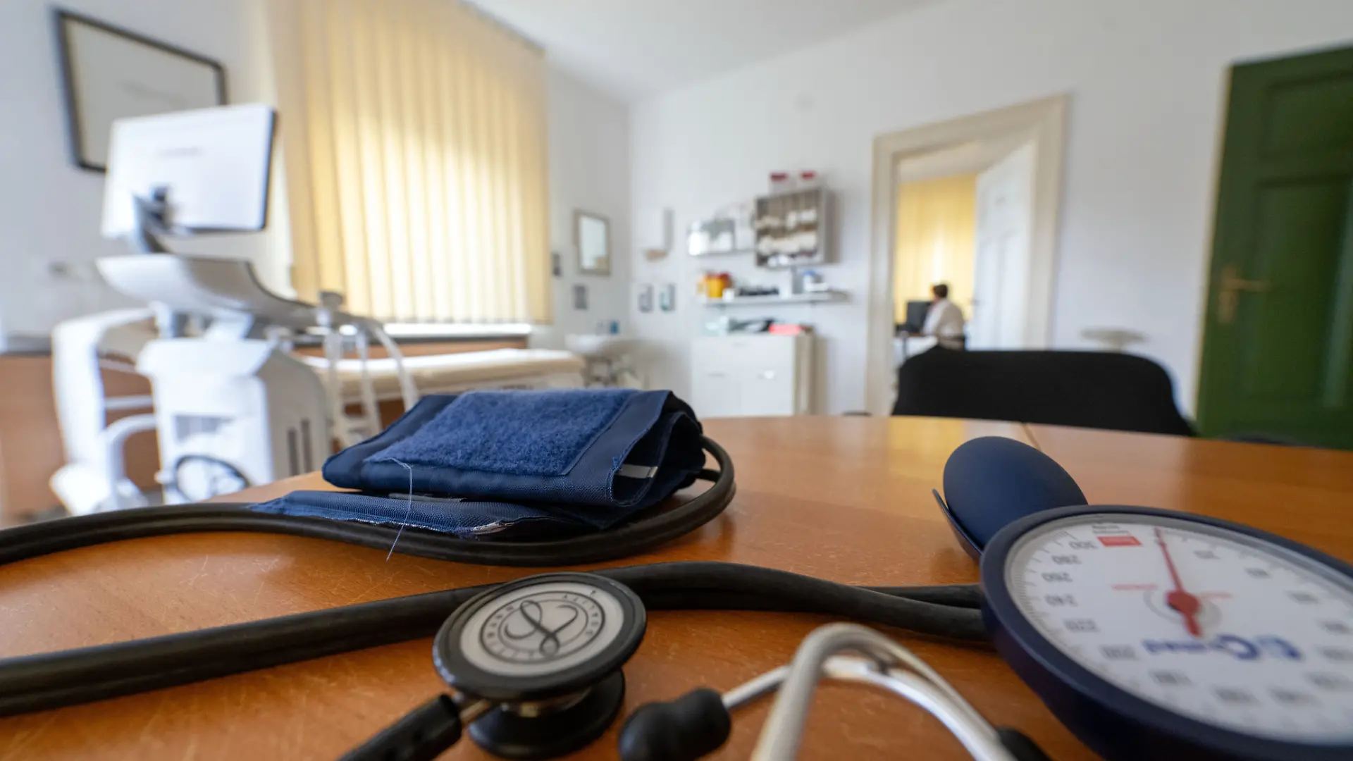 Auf dem Tisch einer Allgemeinarztpraxis liegen ein Stethoskop und eine Manschette zur Blutdruckmessung bereit, während im Nebenzimmer an einem Rechner gearbeitet wird. Am 12. Mai startet der 130. Deutsche Ärztetag in Hannover.