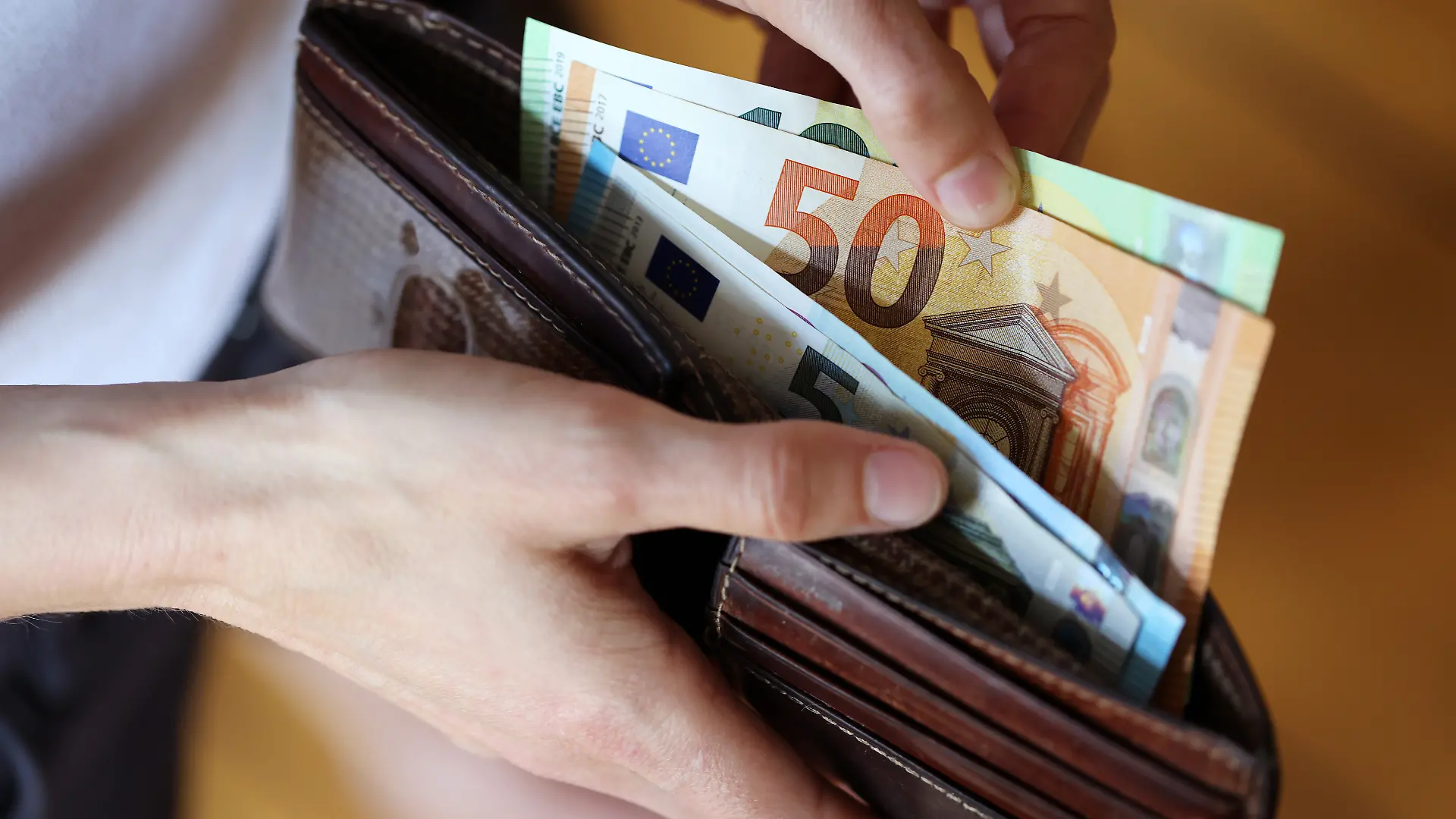 Geldscheine werden aus einem Portemonnaie entnommen.