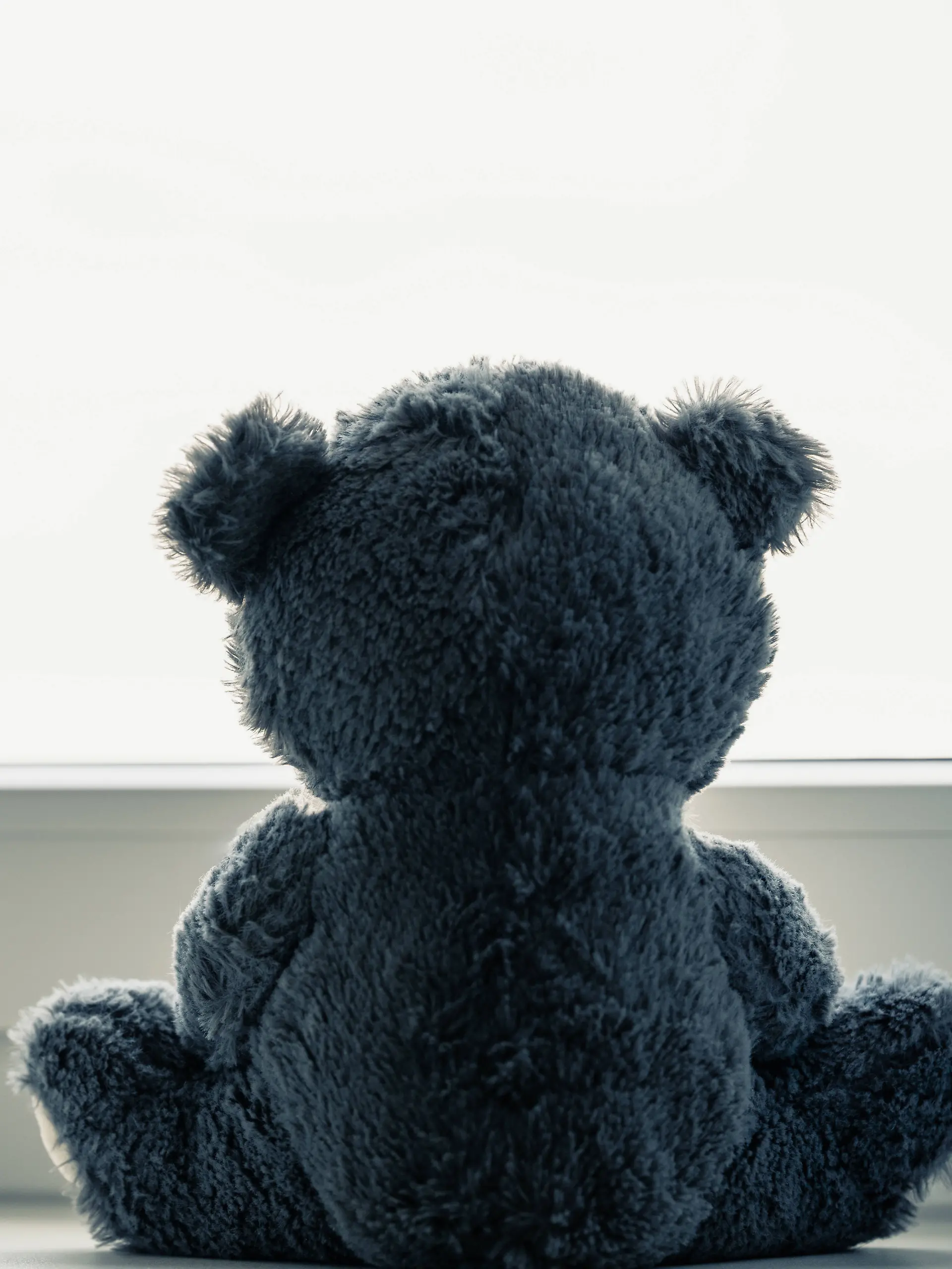 Trauriger Stofftier Teddybär sitzt alleine an einem großen Fenster. 