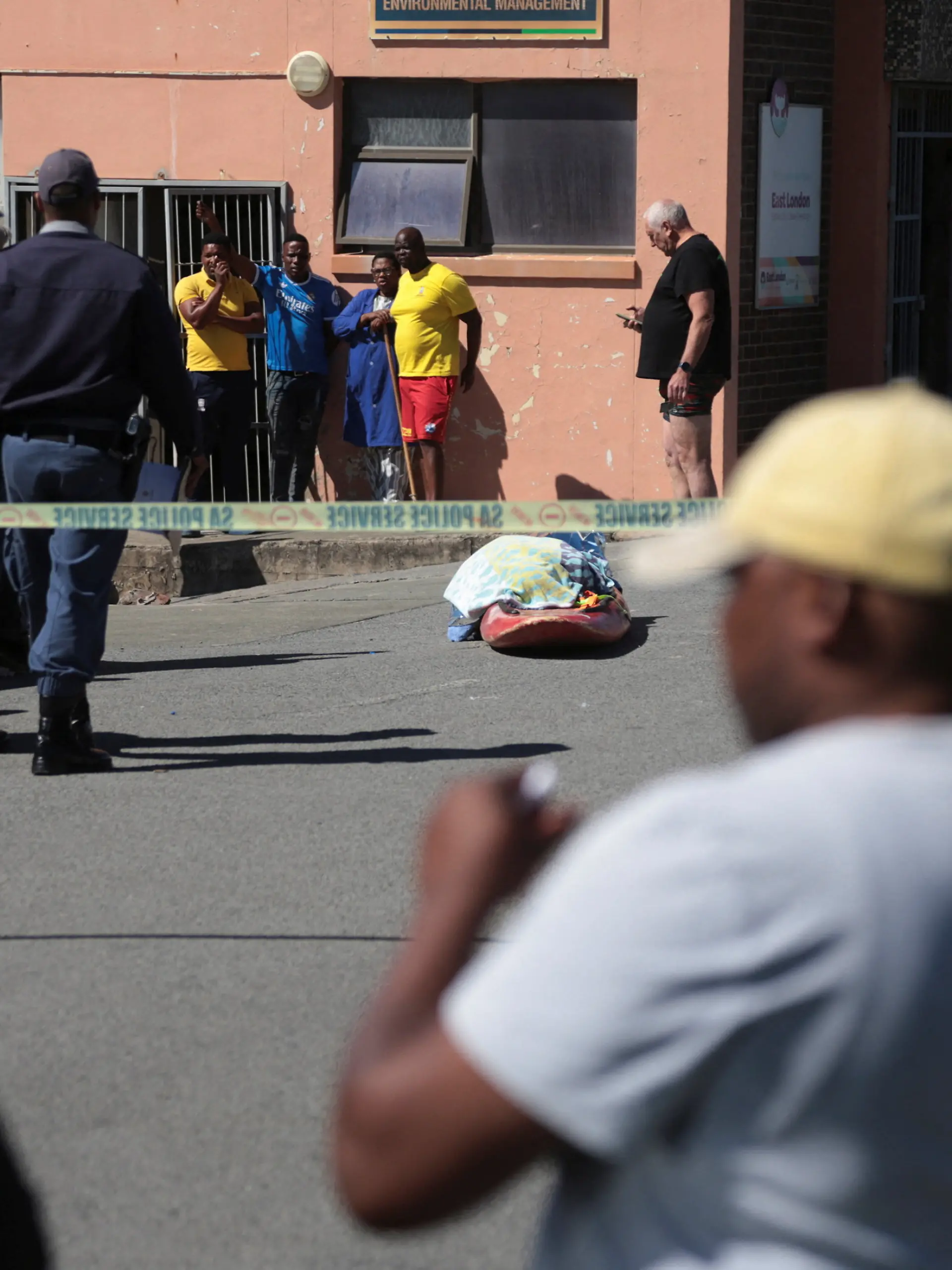 Police officers stand guard as bystanders gather near the covered body of a woman who was killed in a shark attack while swimming off Orient Beach in KuGompo City, Eastern Cape, South Africa, October 20, 2026. REUTERS/Stringer