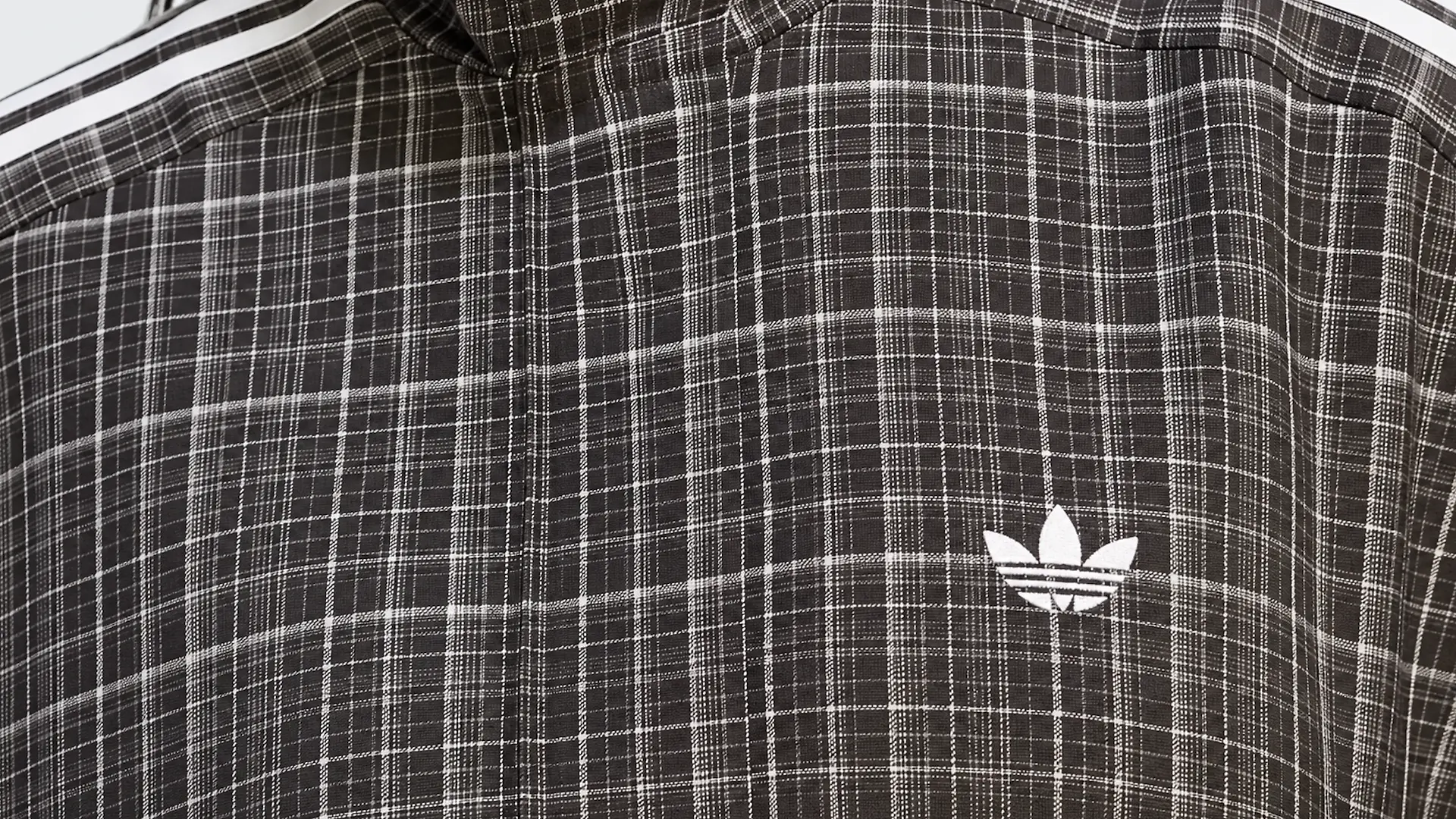 Close-up einer grau-karierten Jacke mit Adidas-Logo