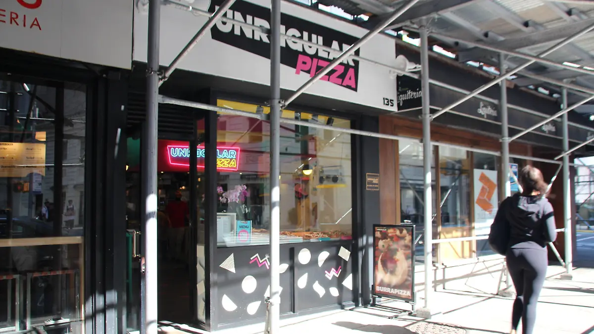 24.06.2021, USA, New York: Eine Frau geht an einer Pizzeria vorbei. In New York kann Pizza jetzt auch ertauscht werden. Während der Corona-Pandemie hatte der aus Italien stammende Lamonaca damit begonnen, bei sich zu Hause Pizza zu machen und diese dann - über durch die sozialen Medien entstandene Verbindungen - gegen andere Dinge zu tauschen, beispielsweise Schokoladenkuchen oder Weinflaschen. Foto: Christina Horsten/dpa +++ dpa-Bildfunk +++