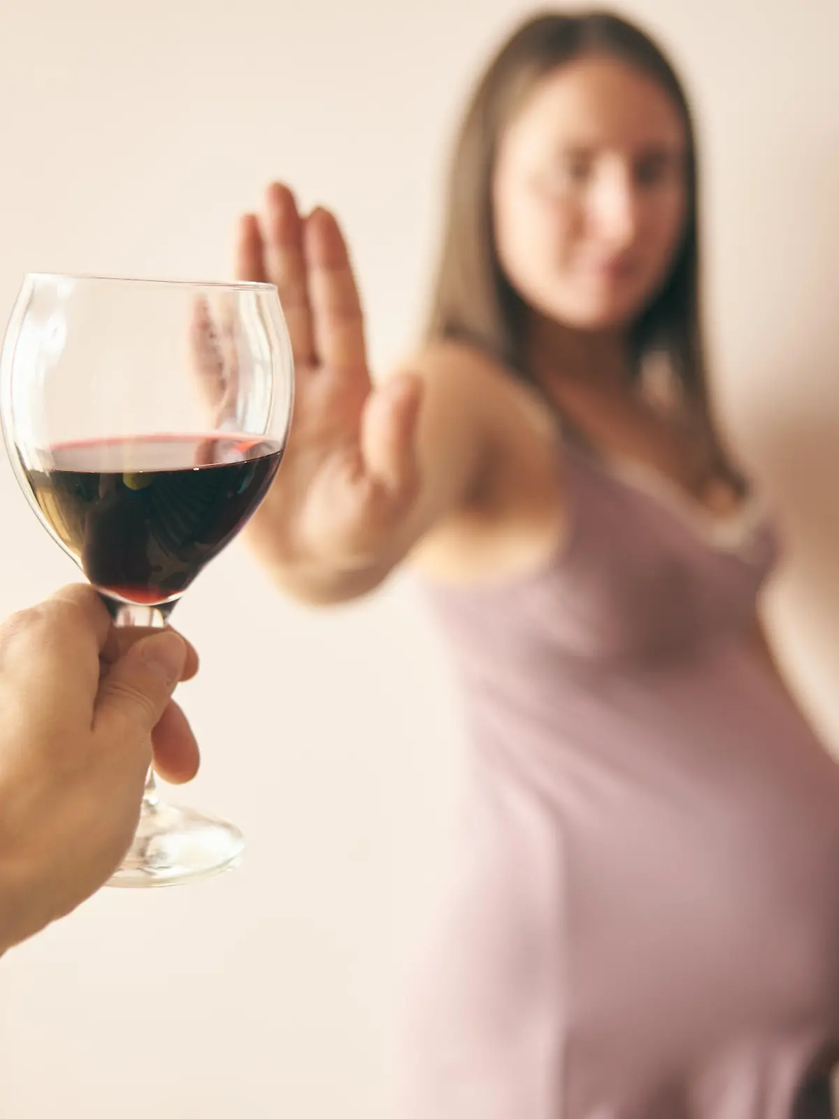 Eine schwangere Frau, der ein Glas Rotwein hingehalten wird, lehnt dieses ab und sagt damit "Nein" zu Alkohol während der Schwangerschaft.