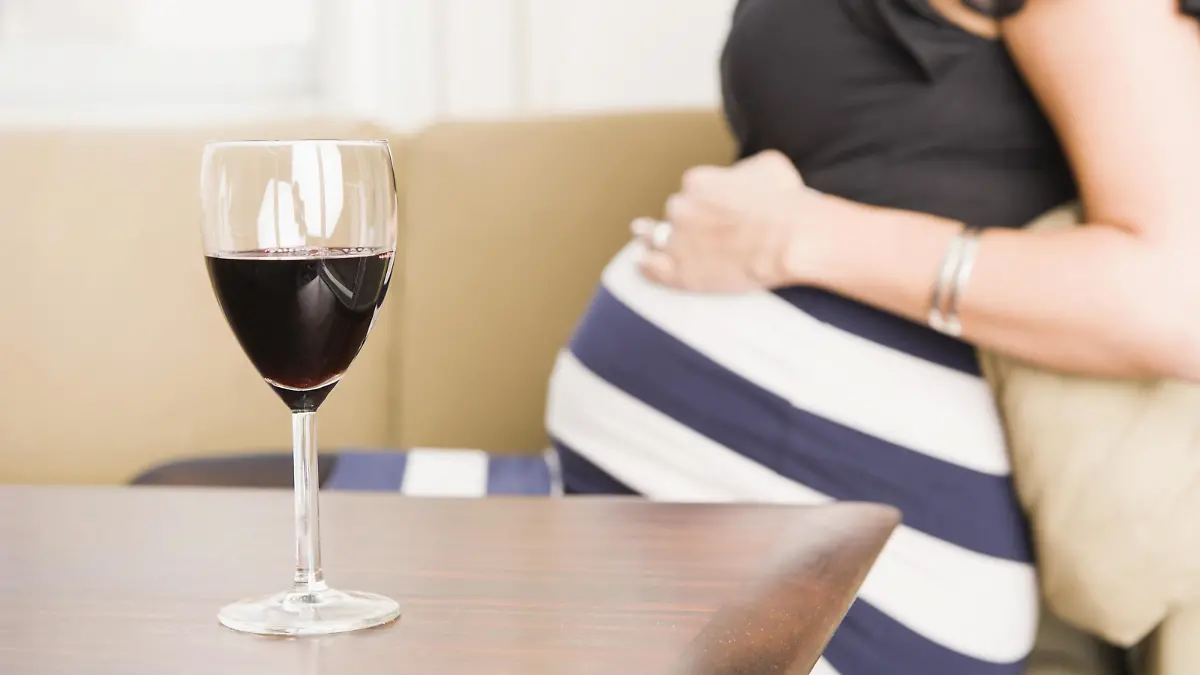 Glas Rotwein auf einem Tisch, schwangere Frau hinten | Verwendung weltweit, Keine Weitergabe an Wiederverkäufer.