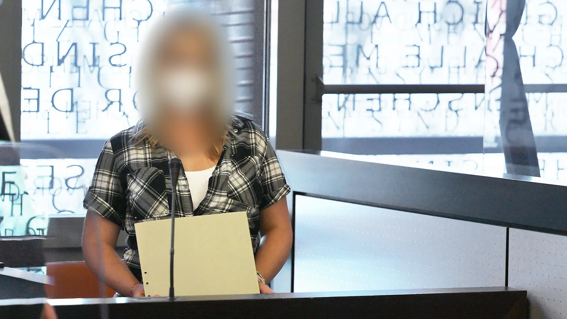14.06.2021, Nordrhein-Westfalen, Wuppertal: Die angeklagte Mutter (r) spricht mit einem ihrer Anwälte - in einer wegen Corona angebrachten Scheibe spiegelt sich das Wort "Gesetz" vom Fenster. Im Fall der fünf getöteten Kinder im nordrhein-westfälischen Solingen hat vor dem Landgericht Wuppertal der Mordprozess gegen deren Mutter begonnen. Foto: Oliver Berg/dpa - ACHTUNG: Die Angeklagte wurde aus rechtlichen Gründen gepixelt +++ dpa-Bildfunk +++
