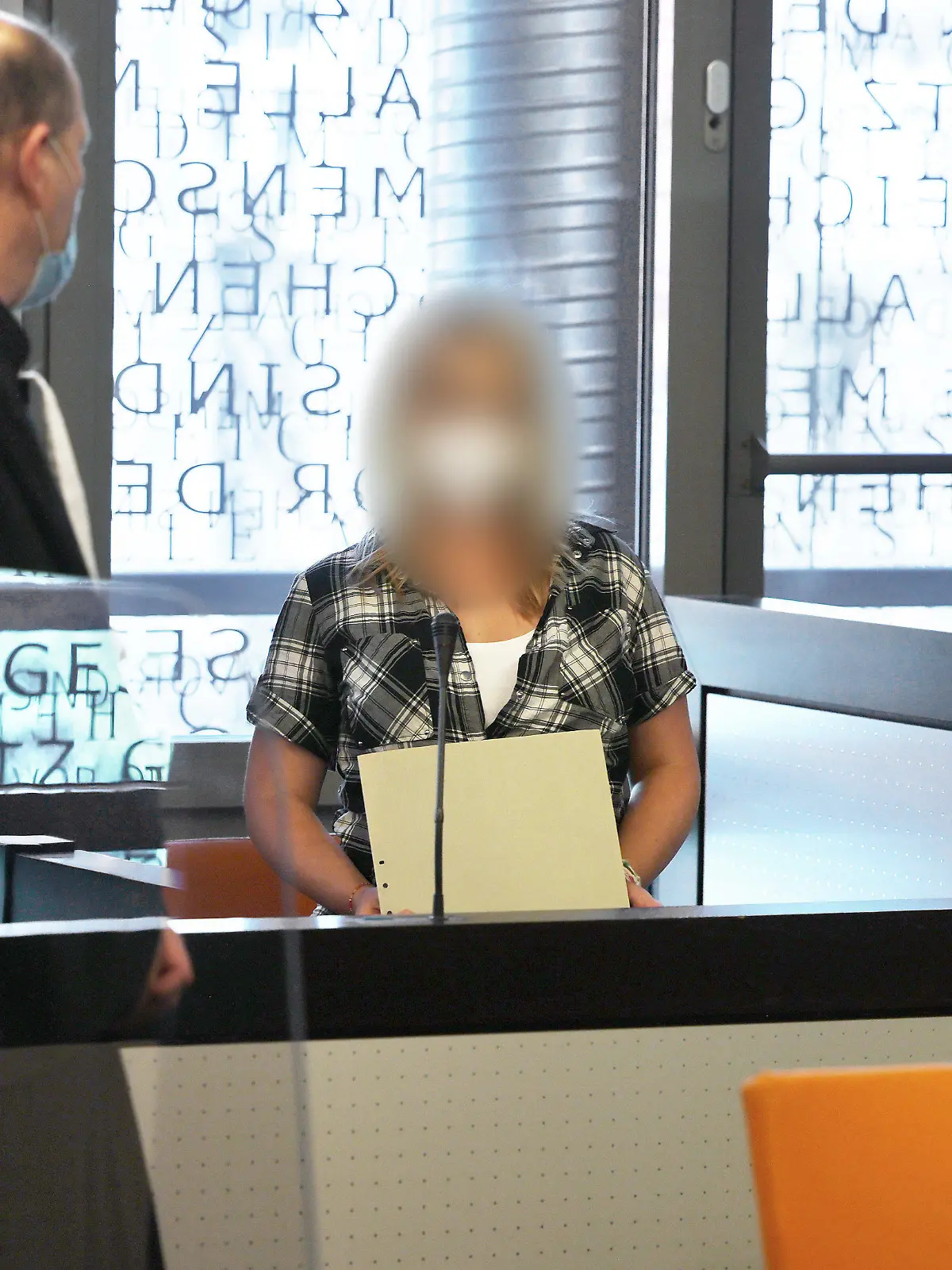 14.06.2021, Nordrhein-Westfalen, Wuppertal: Die angeklagte Mutter (r) spricht mit einem ihrer Anwälte - in einer wegen Corona angebrachten Scheibe spiegelt sich das Wort "Gesetz" vom Fenster. Im Fall der fünf getöteten Kinder im nordrhein-westfälischen Solingen hat vor dem Landgericht Wuppertal der Mordprozess gegen deren Mutter begonnen. Foto: Oliver Berg/dpa - ACHTUNG: Die Angeklagte wurde aus rechtlichen Gründen gepixelt +++ dpa-Bildfunk +++