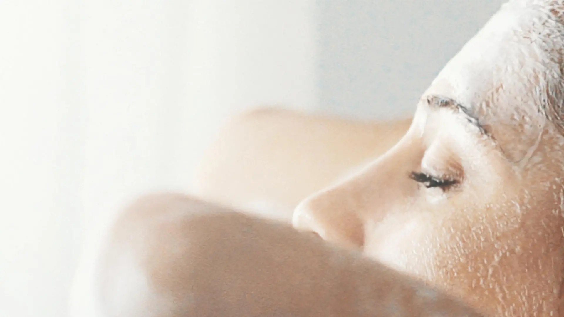 Closeup side view of mid 20's woman completely enjoying washiing her blond colored hair. She's going her finger through soapy hair, faced to the bathroom window.