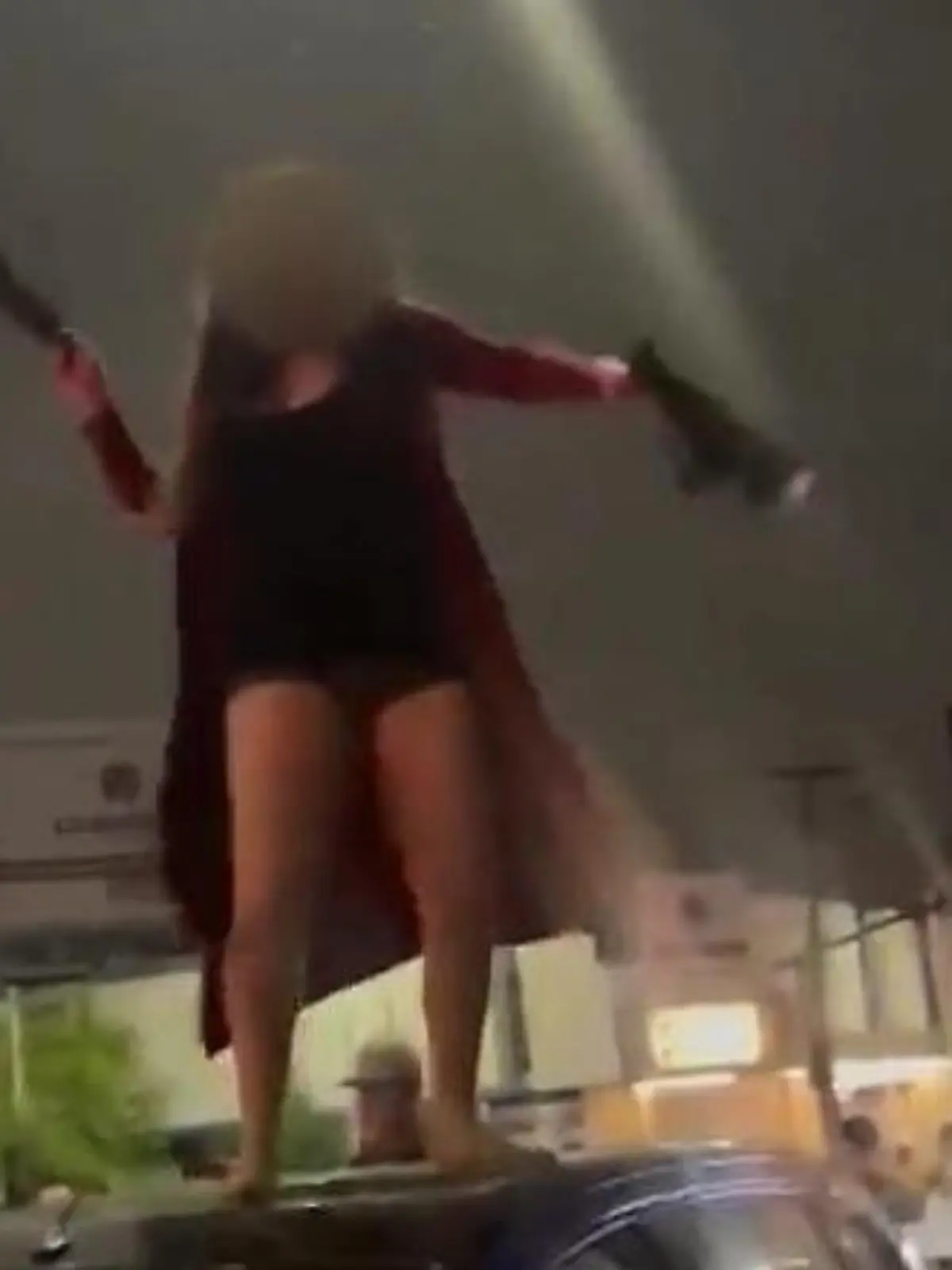 Eine Frau steht auf einem SUV und will gerade ihre Schuhe nach jemandem werfen.