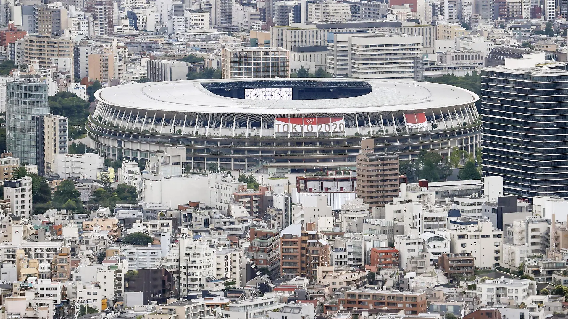 22.06.2021, Japan, Tokio: Ein Banner verkündet auf dem Nationalstadion, einem Austragungsort der Olympischen Spiele und Paralympics in Tokio, unter dem Zeichen der Olympischen Ringe "Tokio 2020". Die Olympischen Spiele 2020 sind die aktuellen Olympischen Sommerspiele und sollen corona-bedingt vom 23. Juli bis zum 8. August 2021 in Tokio stattfinden. Foto: ---/kyodo/dpa +++ dpa-Bildfunk +++