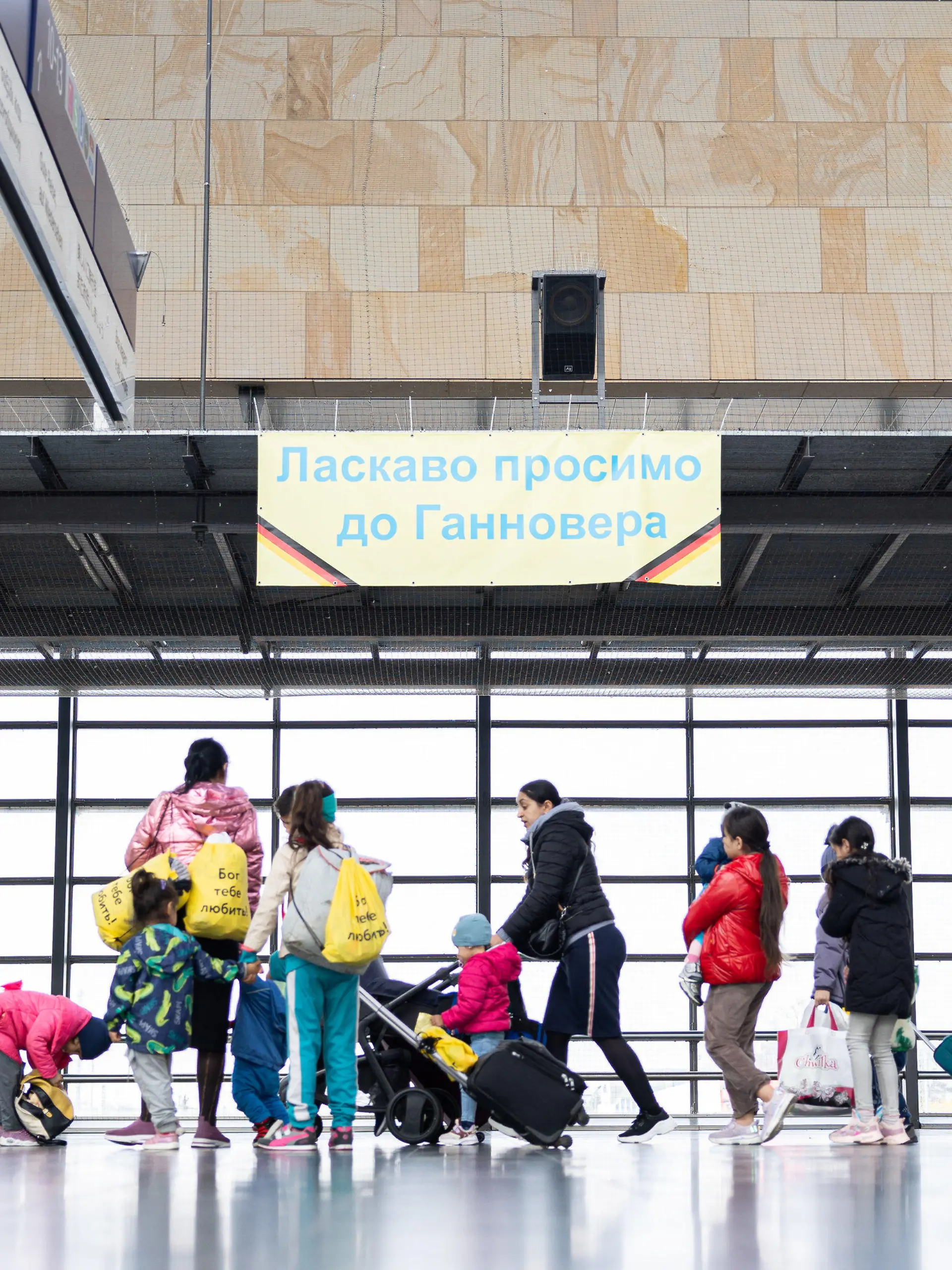 ARCHIV - 15.04.2023, Niedersachsen, Laatzen: Geflüchtete aus der Ukraine gehen durch die Eingangshalle vom Messebahnhof Laatzen. Auf einem Banner im Hintergrund steht «Willkommen in Hannover» auf Ukrainisch. Die Landeshauptstadt Hannover, die Städte Oldenburg und Osnabrück sowie die Landkreise Göttingen, Heidekreis, Uelzen und Osnabrück müssen demnach in dieser Zeit nur noch in Ausnahmefällen weitere Flüchtlinge aufnehmen. (zu dpa «Sieben Regionen müssen fast keine Flüchtlinge mehr aufnehmen») Foto: Michael Matthey/dpa +++ dpa-Bildfunk +++