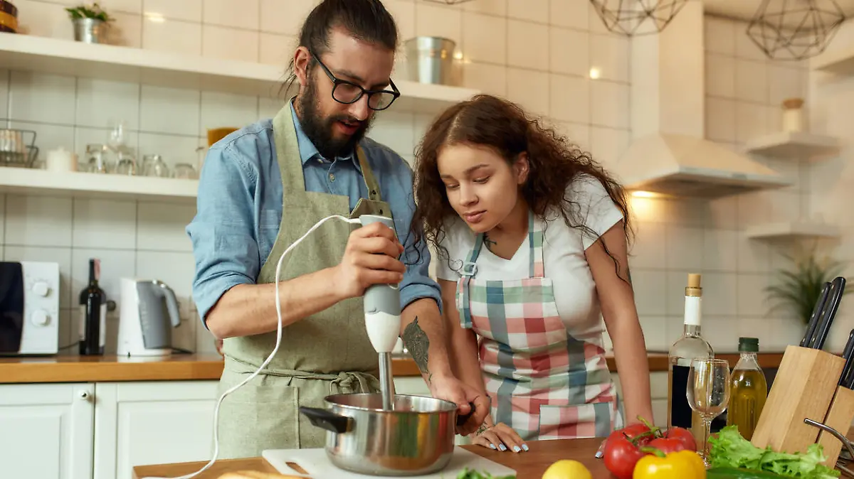 Mann und junge Frau mit dunklen Locken kochen mit Stabmixer