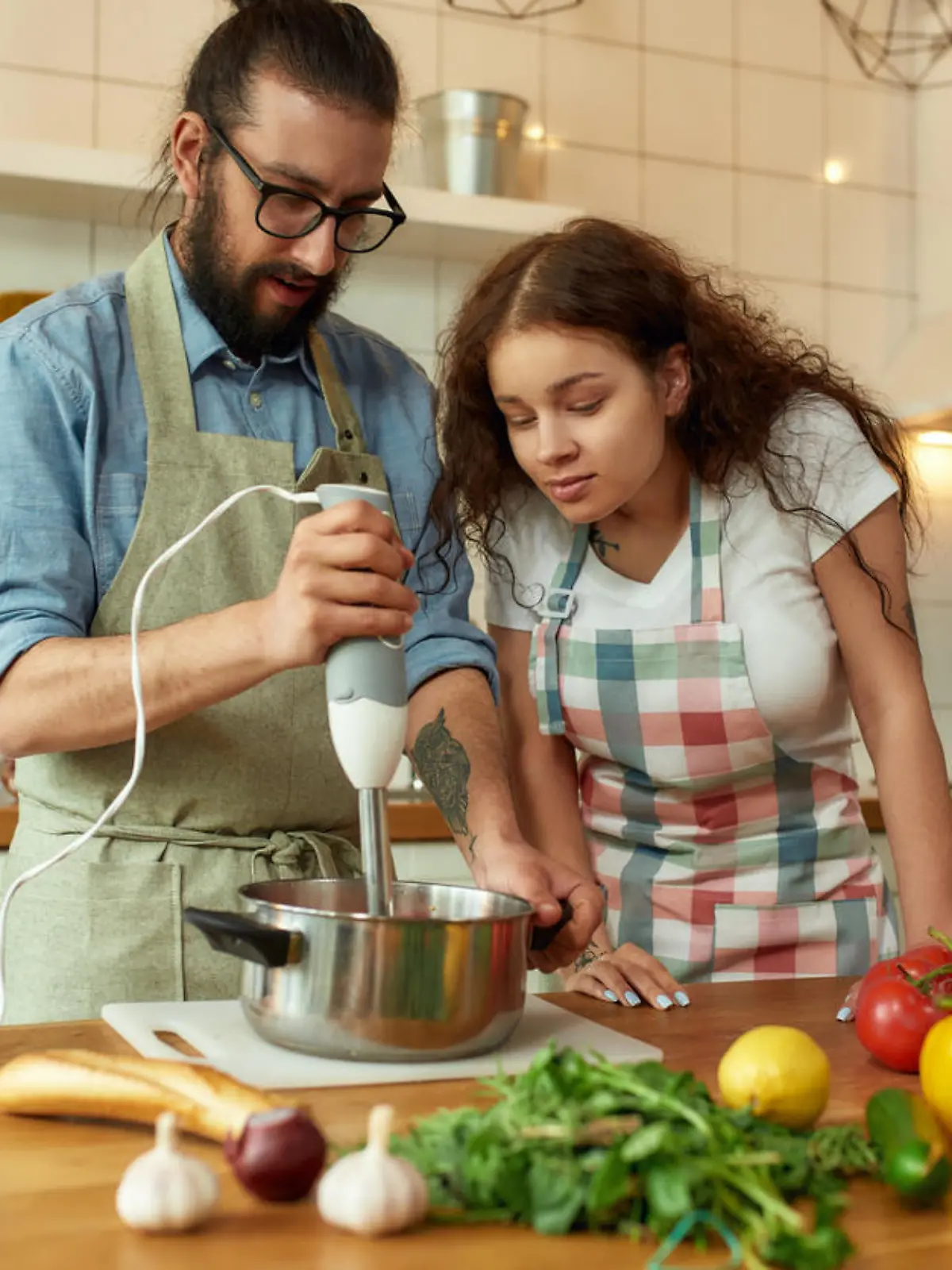Mann und junge Frau mit dunklen Locken kochen mit Stabmixer