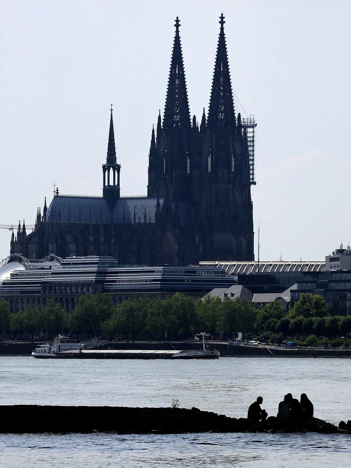 17.06.2021, Nordrhein-Westfalen, Köln: Menschen sitzen am Rheinufer im Schatten unter einer Brücke. Das Wetter in Nordrhein-Westfalen ist hochsommerlich. Foto: Oliver Berg/dpa +++ dpa-Bildfunk +++