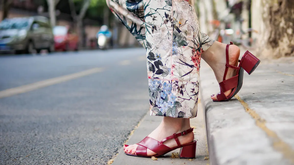 Close up on girl's feet wearing red sandals in the city, urban road background.