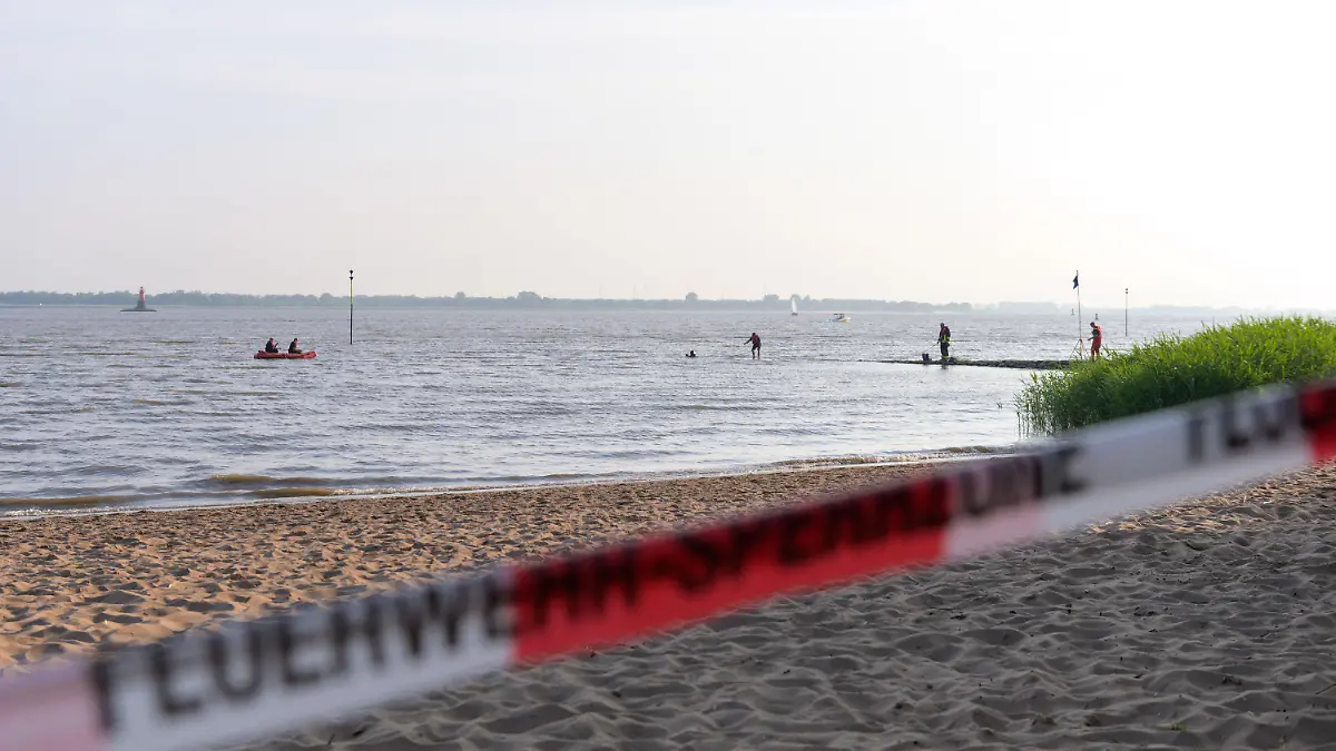 19.06.2021, Schleswig-Holstein, Kollmar: Feuerwehrleute suchen mit Schlauchboot und Tauchern nahe dem abgesperrten Badestrand. In der Elbe bei Kollmar (Kreis Steinburg) suchen Einsatzkräfte nach einem neunjährigen Mädchen, das dort baden gegangen war. Nach aktuellem Stand werde auch ein Erwachsener vermisst, sagte ein Sprecher der Feuerwehr am Samstagabend. Foto: Jonas Walzberg/dpa +++ dpa-Bildfunk +++