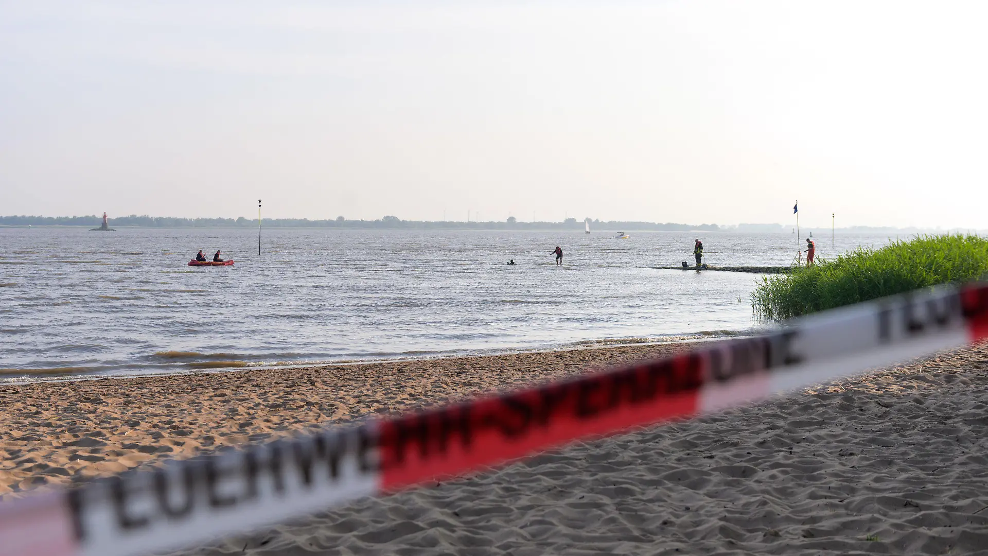 19.06.2021, Schleswig-Holstein, Kollmar: Feuerwehrleute suchen mit Schlauchboot und Tauchern nahe dem abgesperrten Badestrand. In der Elbe bei Kollmar (Kreis Steinburg) suchen Einsatzkräfte nach einem neunjährigen Mädchen, das dort baden gegangen war. Nach aktuellem Stand werde auch ein Erwachsener vermisst, sagte ein Sprecher der Feuerwehr am Samstagabend. Foto: Jonas Walzberg/dpa +++ dpa-Bildfunk +++