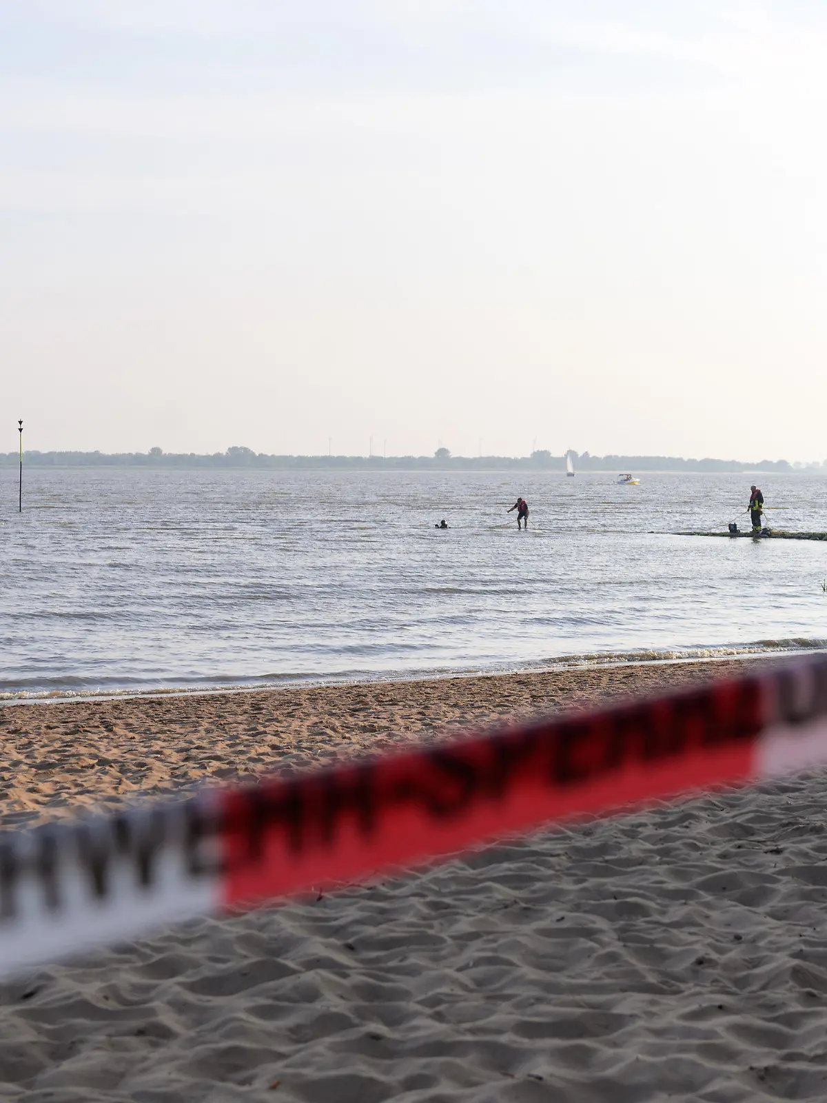 19.06.2021, Schleswig-Holstein, Kollmar: Feuerwehrleute suchen mit Schlauchboot und Tauchern nahe dem abgesperrten Badestrand. In der Elbe bei Kollmar (Kreis Steinburg) suchen Einsatzkräfte nach einem neunjährigen Mädchen, das dort baden gegangen war. Nach aktuellem Stand werde auch ein Erwachsener vermisst, sagte ein Sprecher der Feuerwehr am Samstagabend. Foto: Jonas Walzberg/dpa +++ dpa-Bildfunk +++