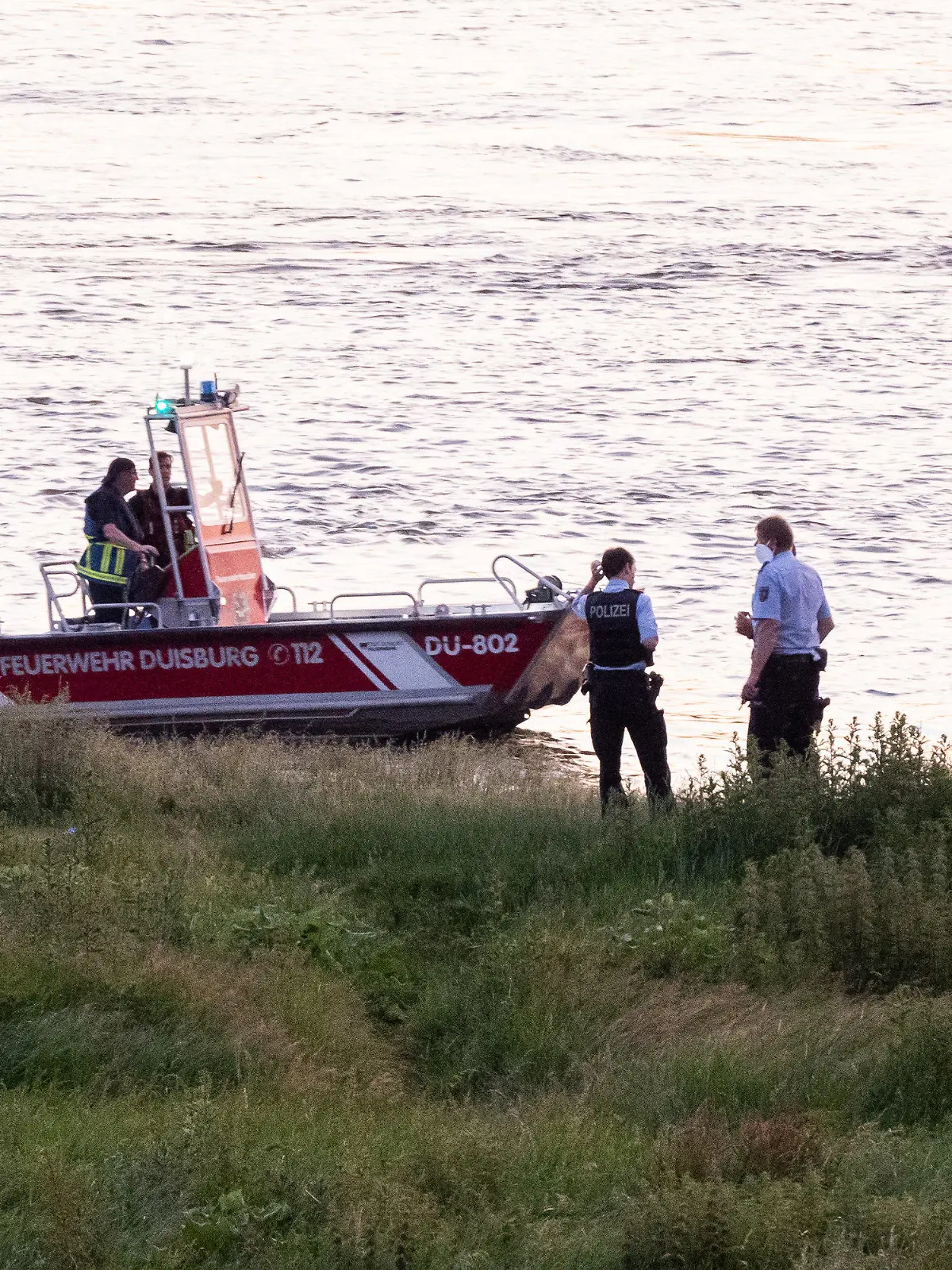 16.06.2021, Nordrhein-Westfalen, Duisburg: Einsatzkräfte der Polizei, Feuerwehr und DRLG arbeiten am Ufer des Rheins. Nach einem möglichen Badeunfall ist eine Person gerettet worden. Zwei weitere werden noch vermisst. Foto: Marcel Kusch/dpa +++ dpa-Bildfunk +++