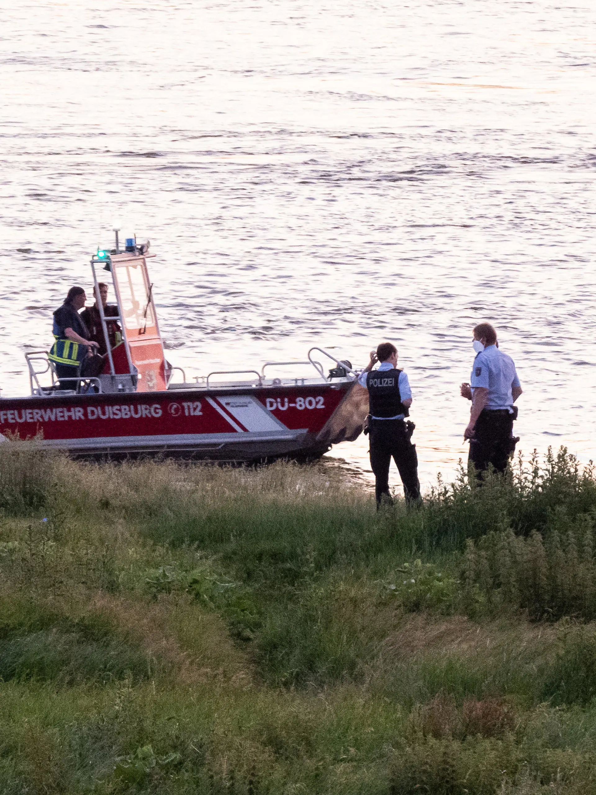 16.06.2021, Nordrhein-Westfalen, Duisburg: Einsatzkräfte der Polizei, Feuerwehr und DRLG arbeiten am Ufer des Rheins. Nach einem möglichen Badeunfall ist eine Person gerettet worden. Zwei weitere werden noch vermisst. Foto: Marcel Kusch/dpa +++ dpa-Bildfunk +++